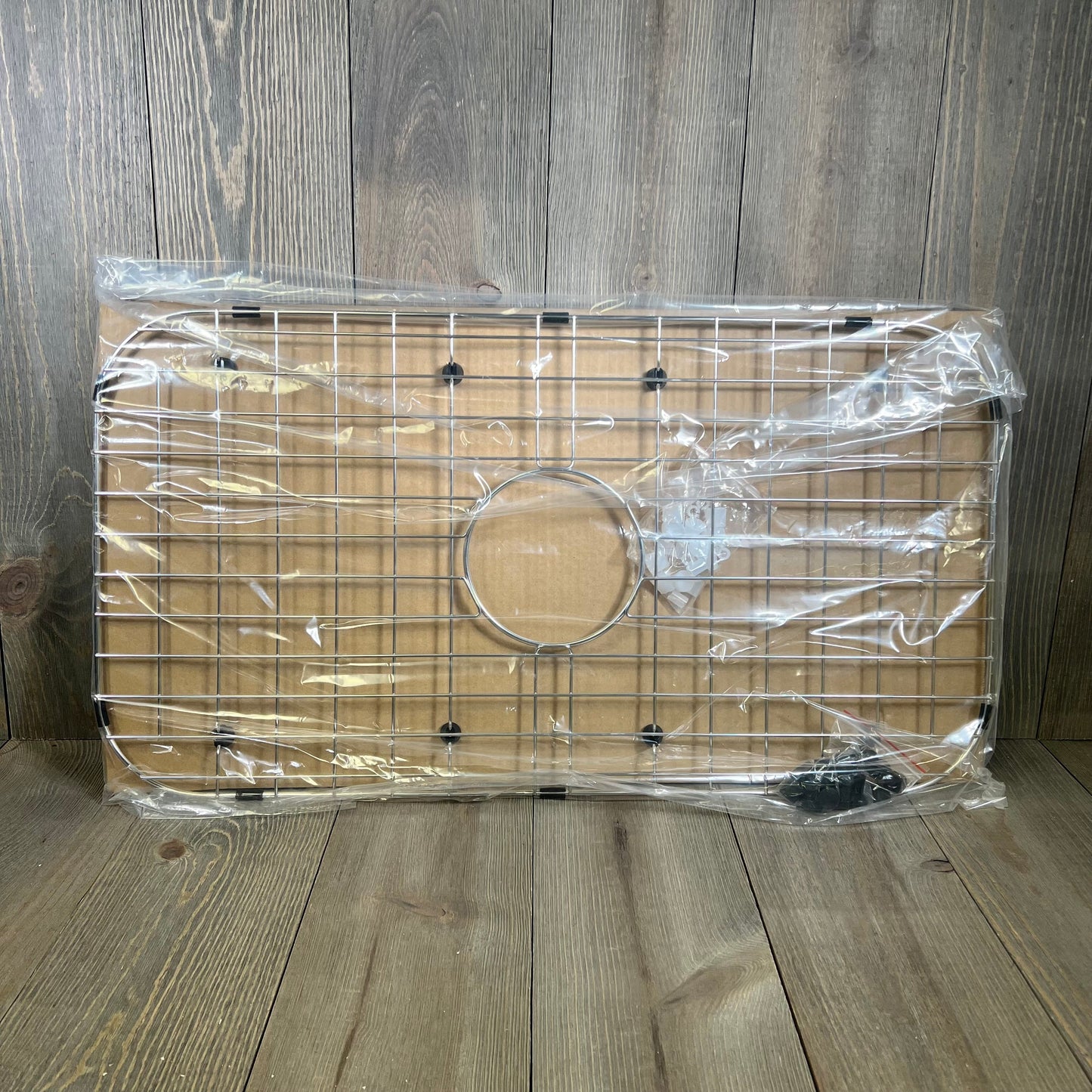 Stainless steel sink protector grid with drain opening, Serene Valley 26-1/16" x 14-1/16", packaged on wooden background.