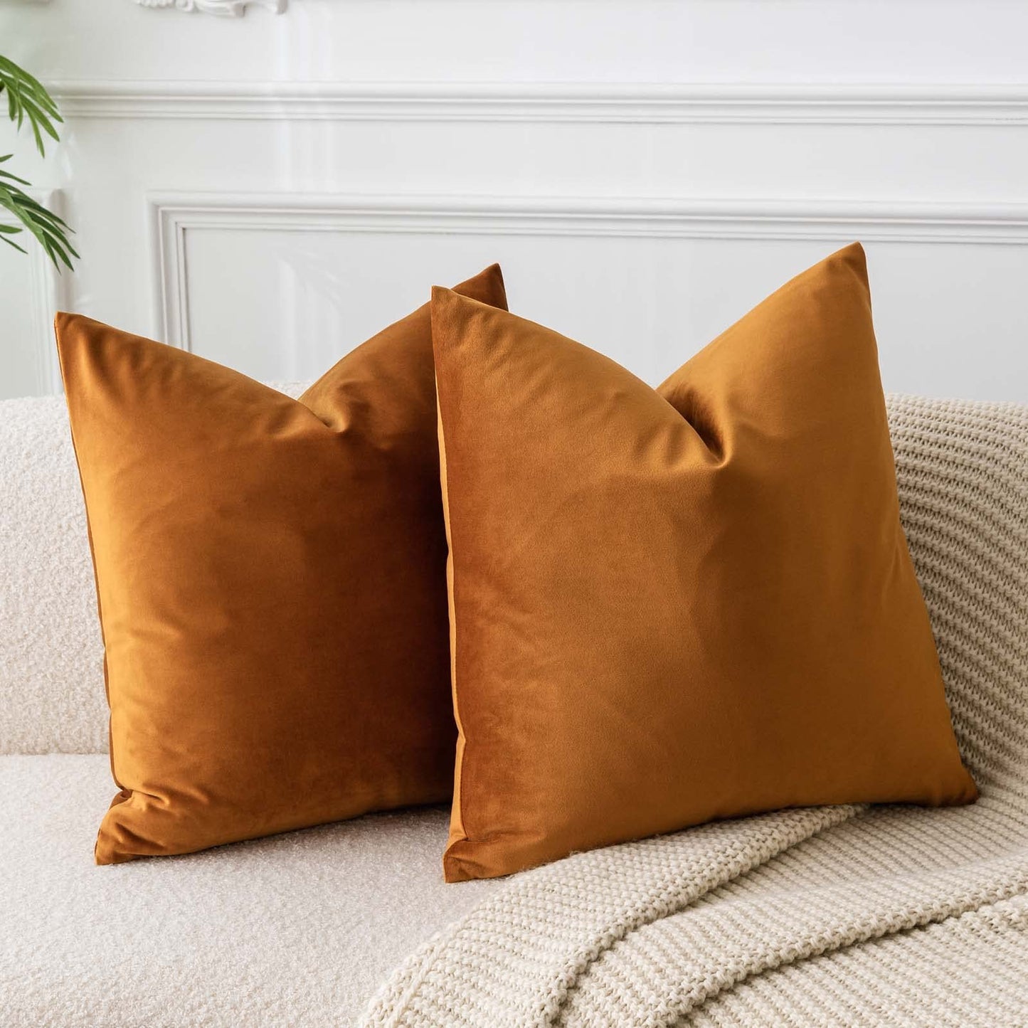 Set of two rust velvet throw pillow covers on a cream sofa, perfect for living room decor and luxury comfort.