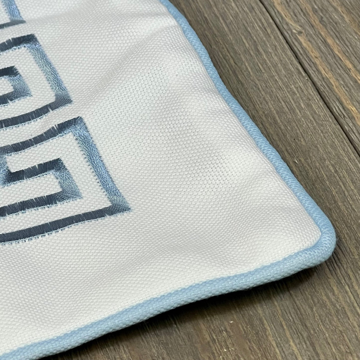 Close-up of Hofdeco pillow cover featuring baby blue Greek key embroidery with piping, ideal for outdoor decor.