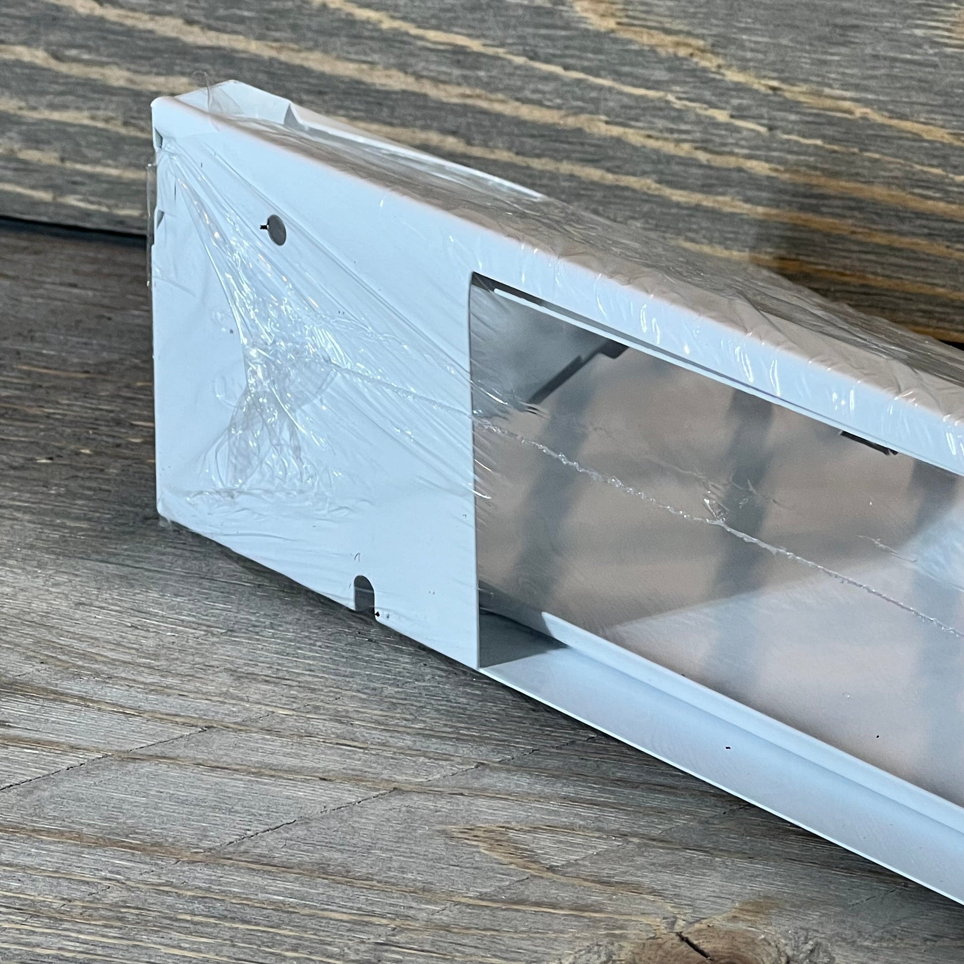 White Blulu baseboard vent cover in packaging, showcasing modern design and durable material on a wooden surface.