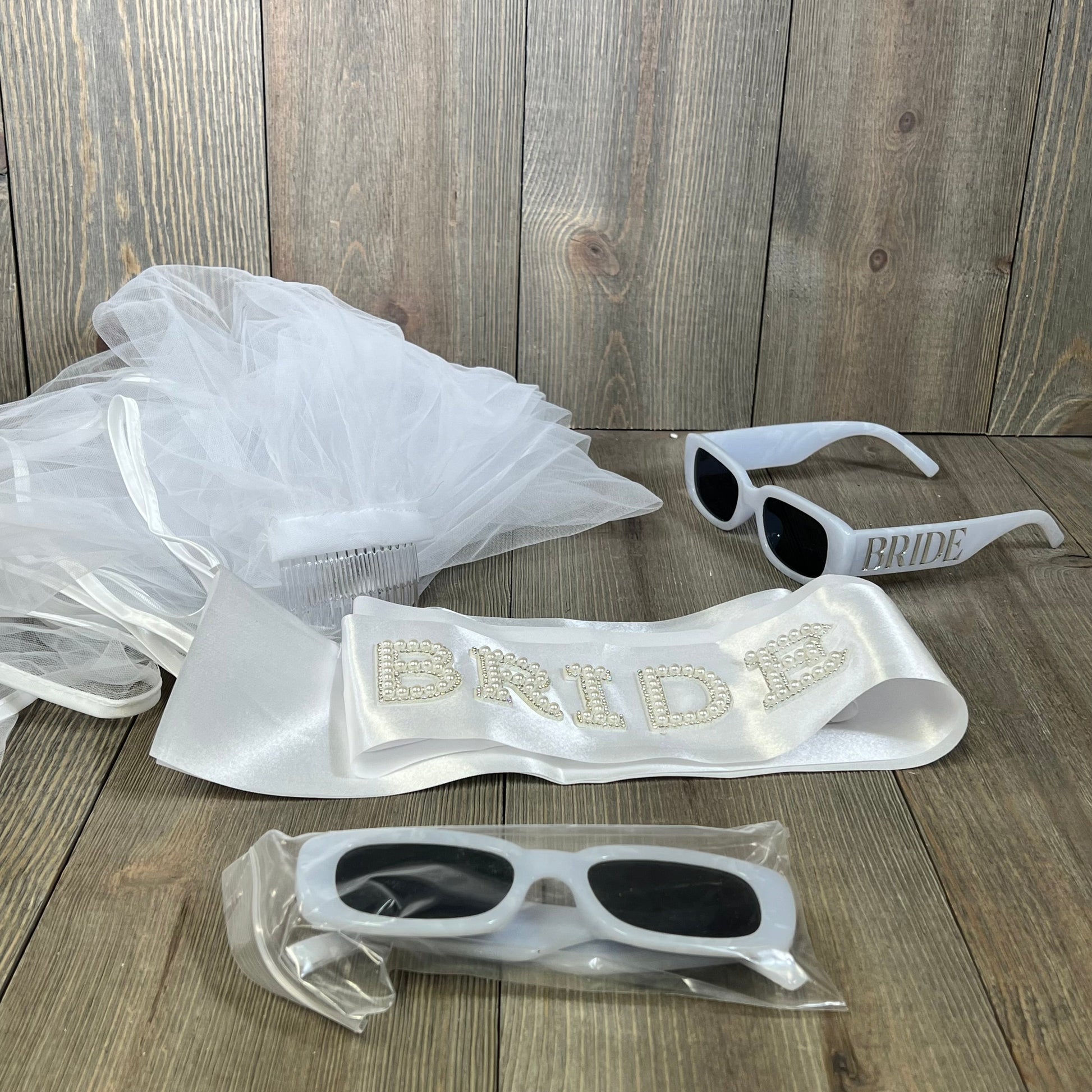 Elegant wedding package featuring bride sash, white veil, and stylish sunglasses on wood background. Perfect for bridal celebrations.