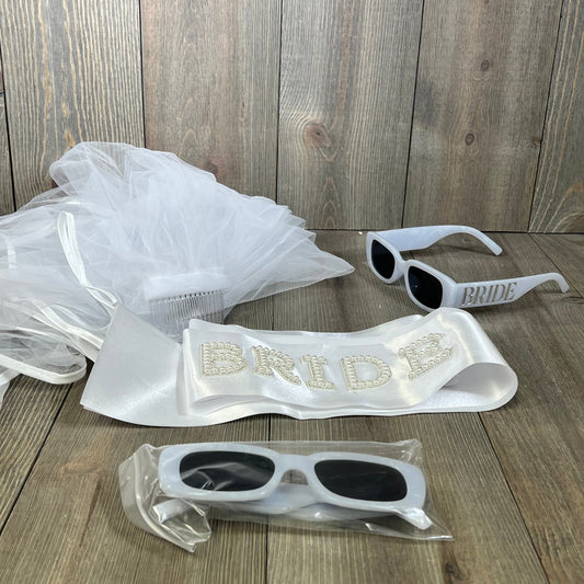 Elegant wedding package featuring bride sash, white veil, and stylish sunglasses on wood background. Perfect for bridal celebrations.
