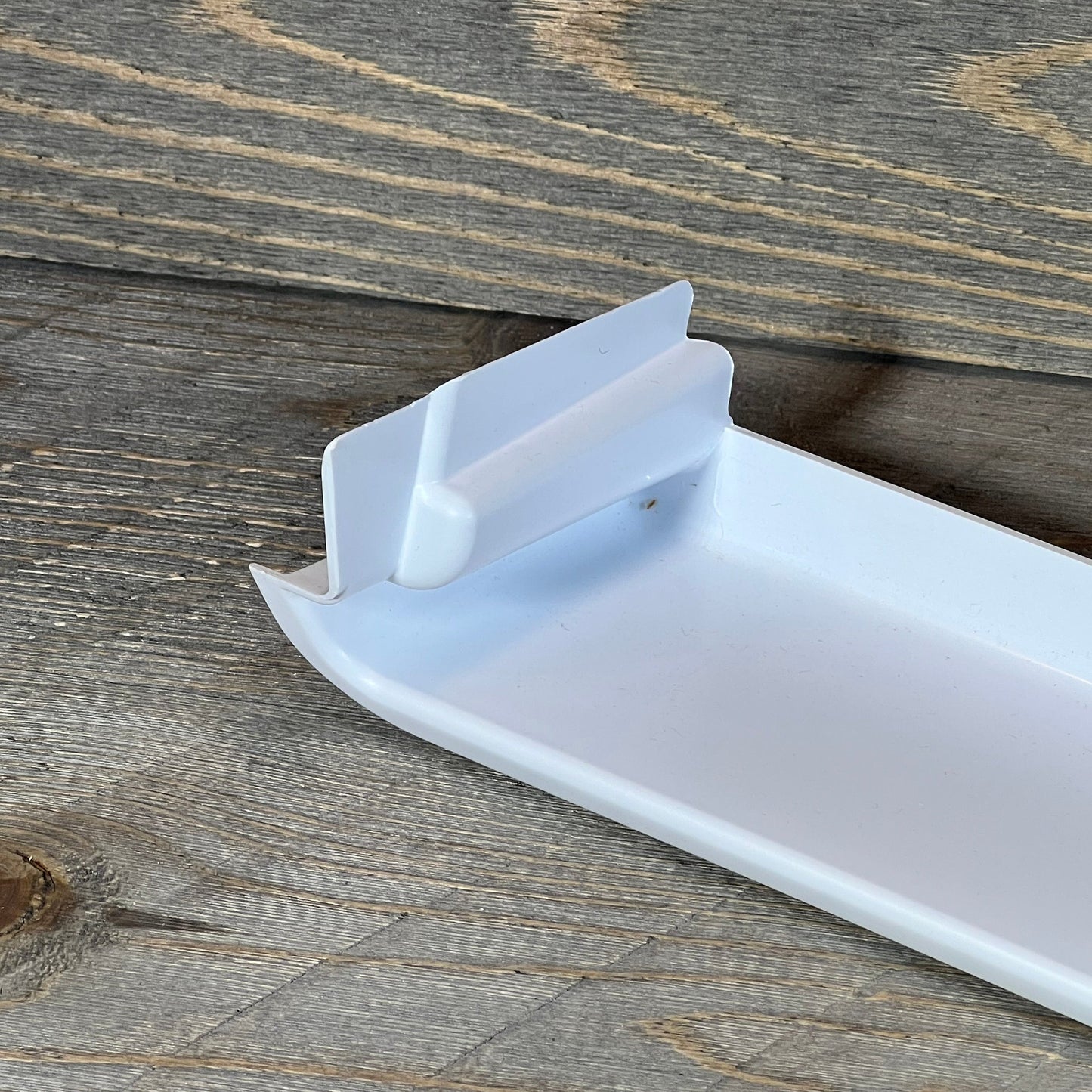 White Frigidaire refrigerator door shelf bin for enhanced storage on rustic wood background.