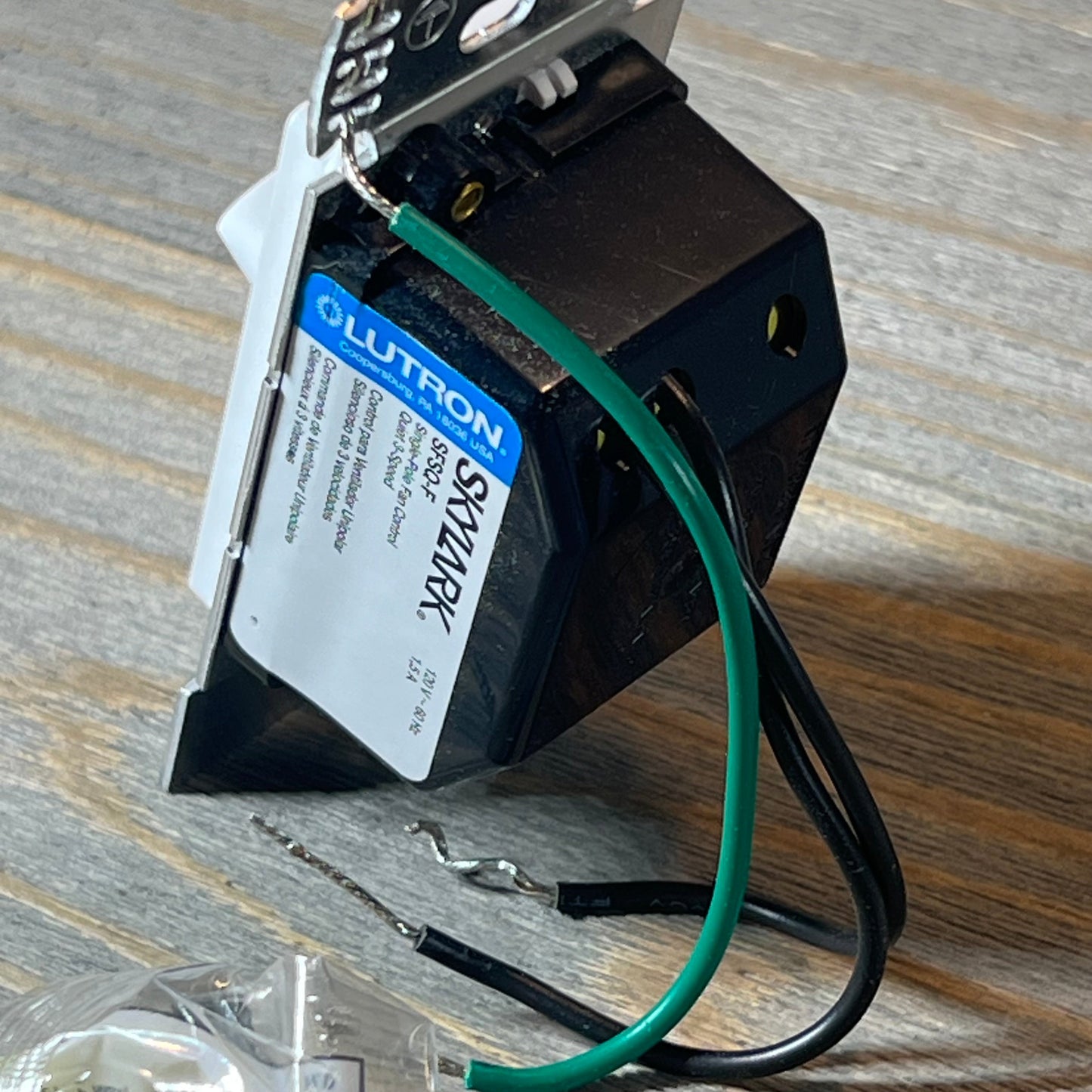 White Lutron Skylark fan control SFSQ-F-WH with wiring, set against a wooden surface.