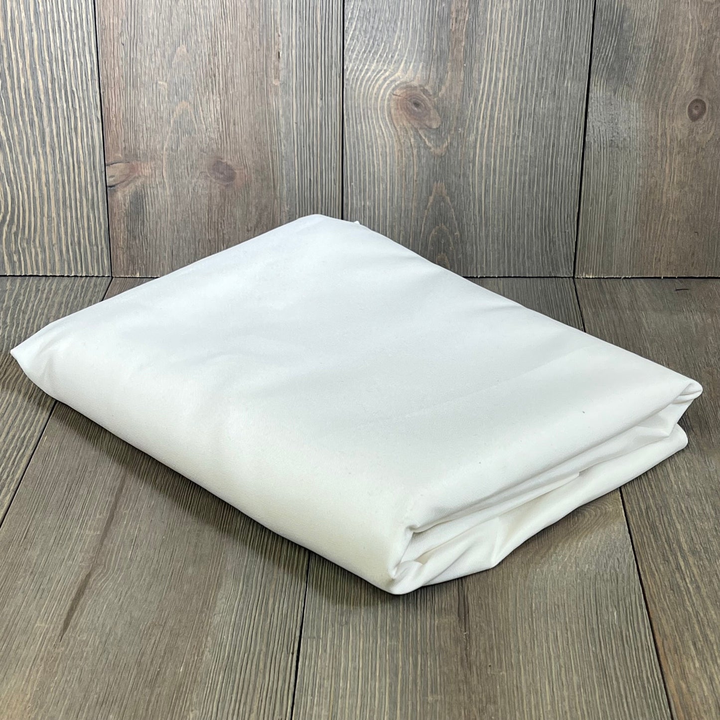 Folded white oval tablecloth on wooden background, showcasing rustic faux linen texture, ideal for farmhouse dining.