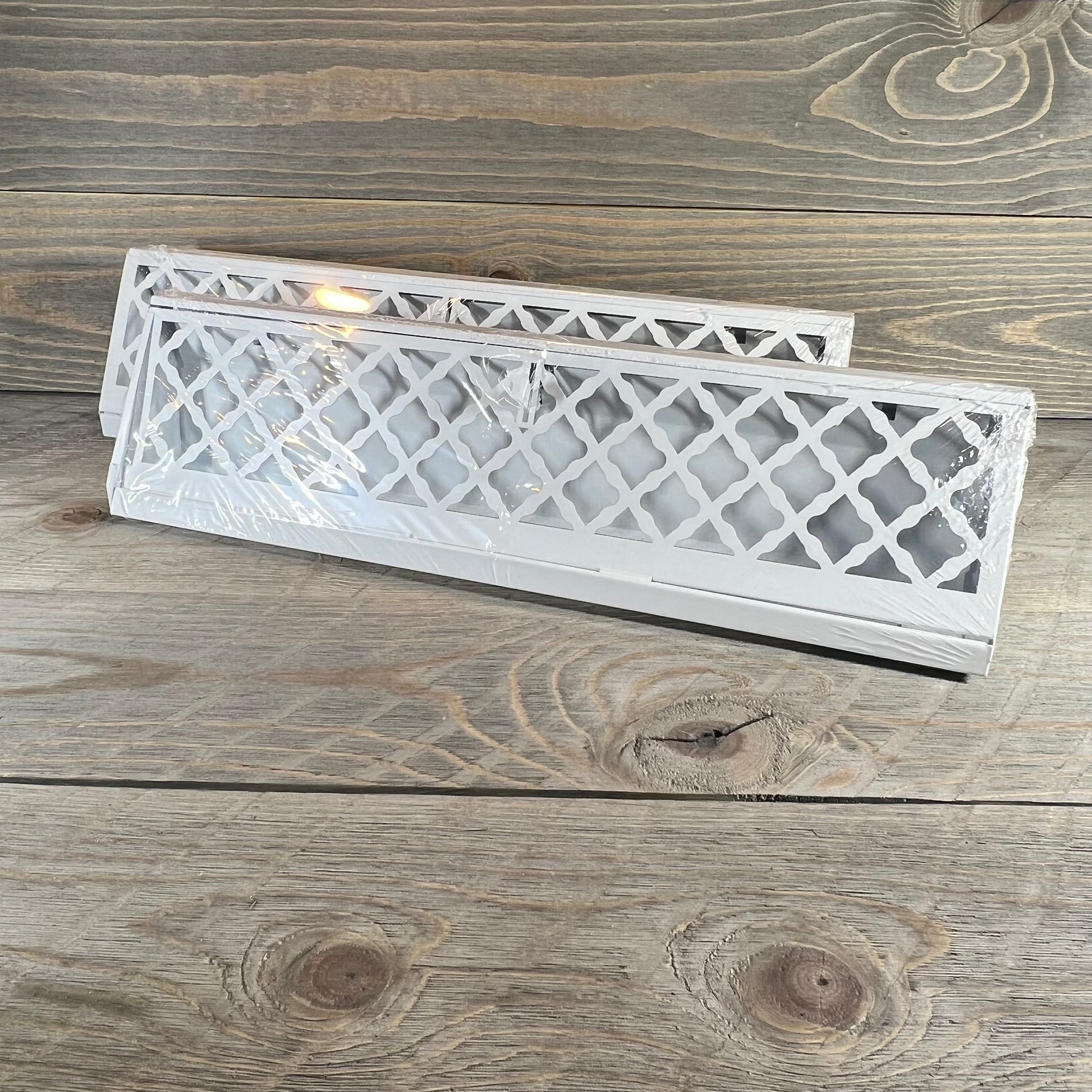 White vent covers with modern lattice design for baseboard use on wooden surface, 18-inch size, packaged.