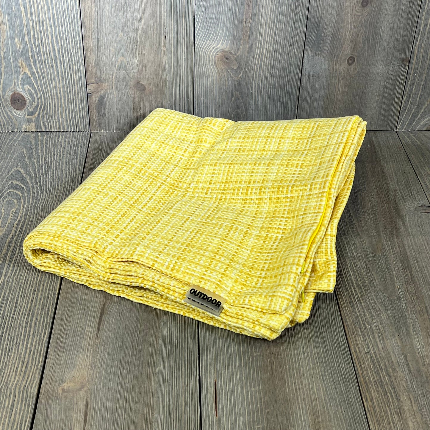 Yellow waterproof throw pillow cover folded on rustic wooden background, perfect for outdoor farmhouse decor.