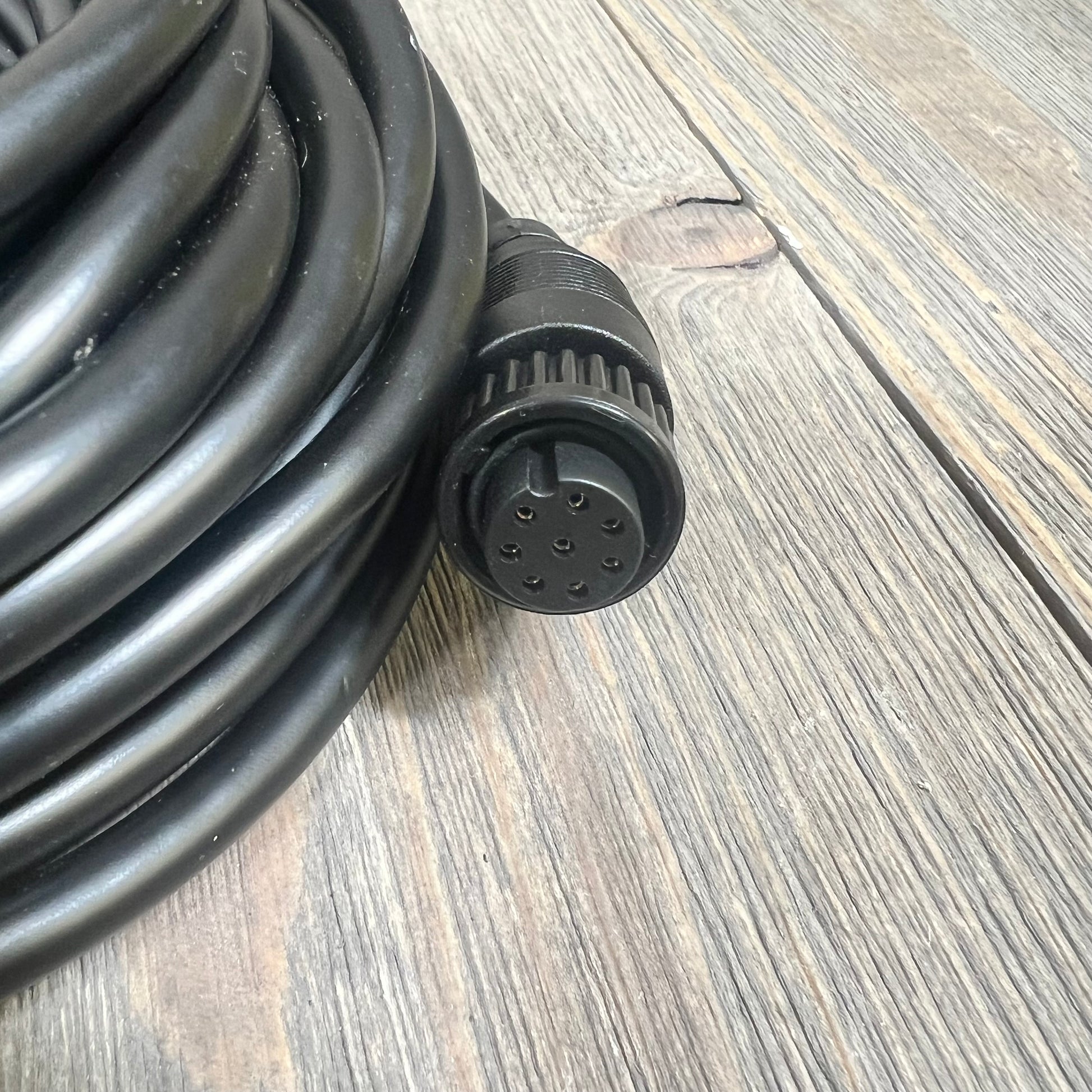 Alt text: Coiled black replacement cable with a multi-pin connector on a wooden surface.