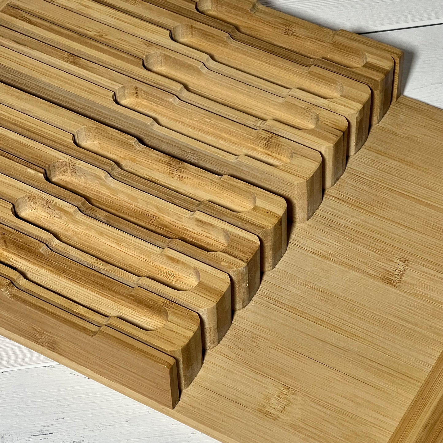 Bamboo in-drawer knife block organizer with slots for 16 knives and a sharpener on a white wooden surface.