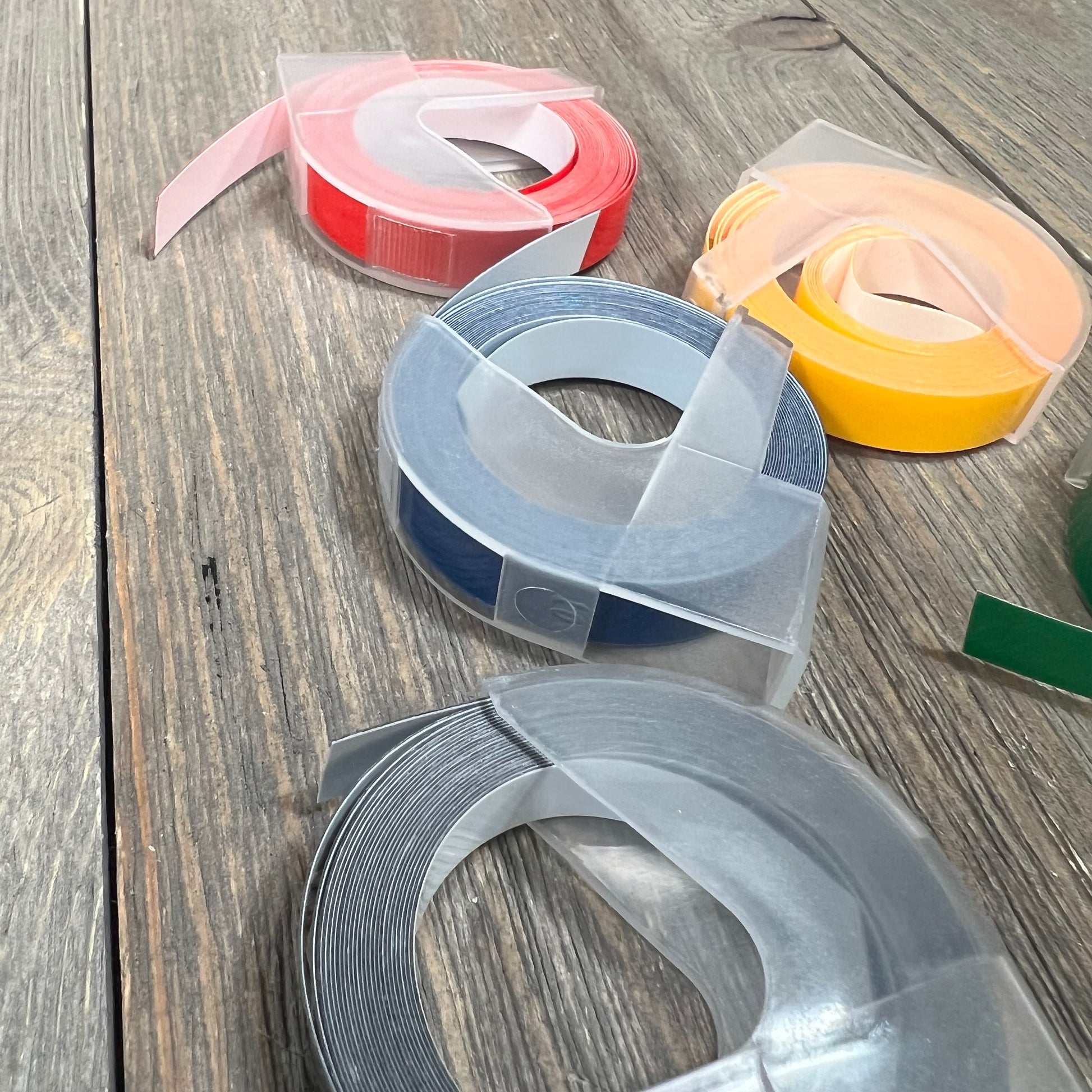 Embossing label tape rolls in various colors for Dymo label makers on a wooden surface.
