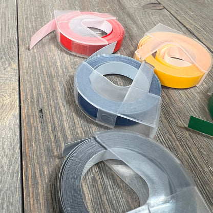 Embossing label tape rolls in various colors for Dymo label makers on a wooden surface.
