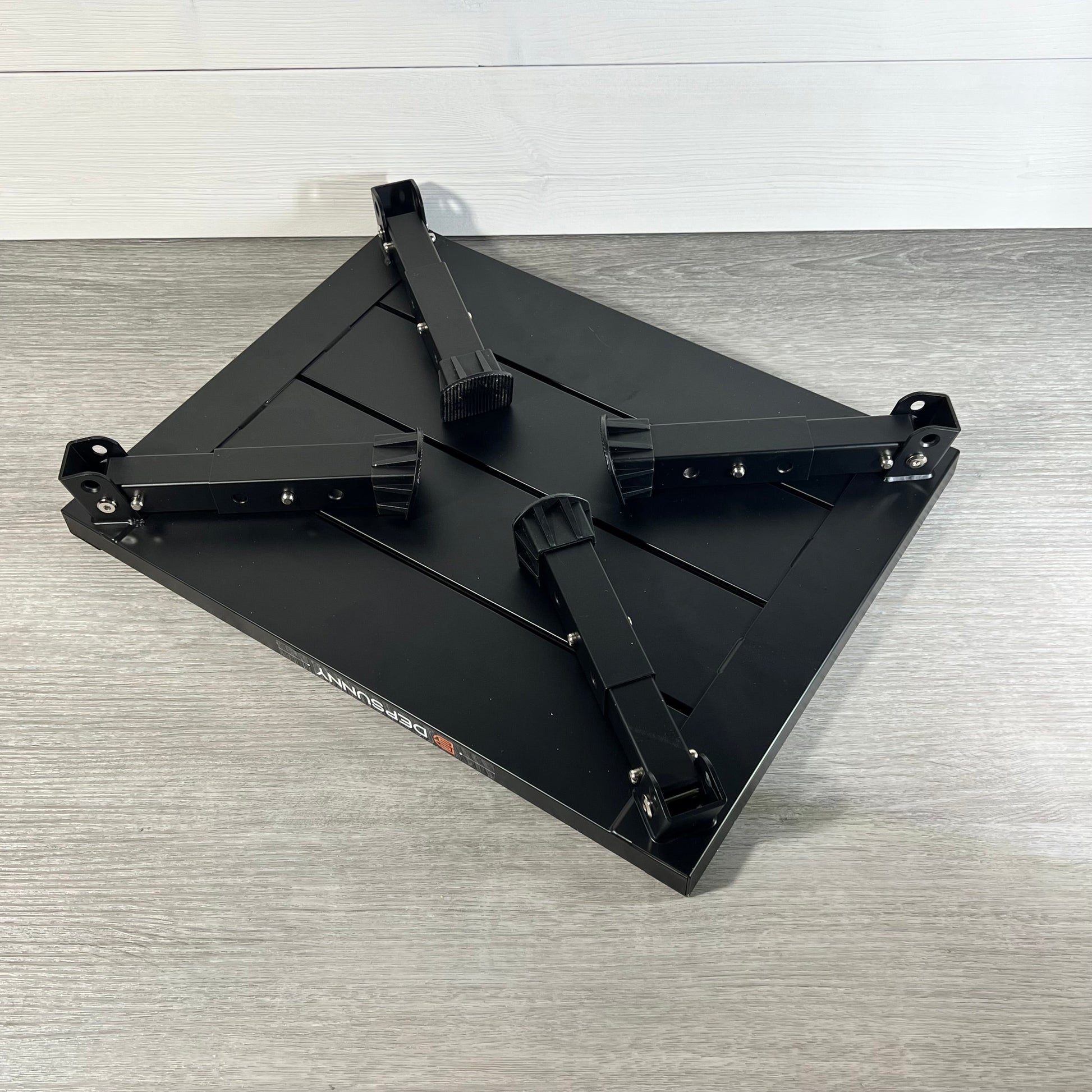Adjustable aluminum RV step with foldable legs, non-slip rubber feet, and durable black finish on a wooden floor background.