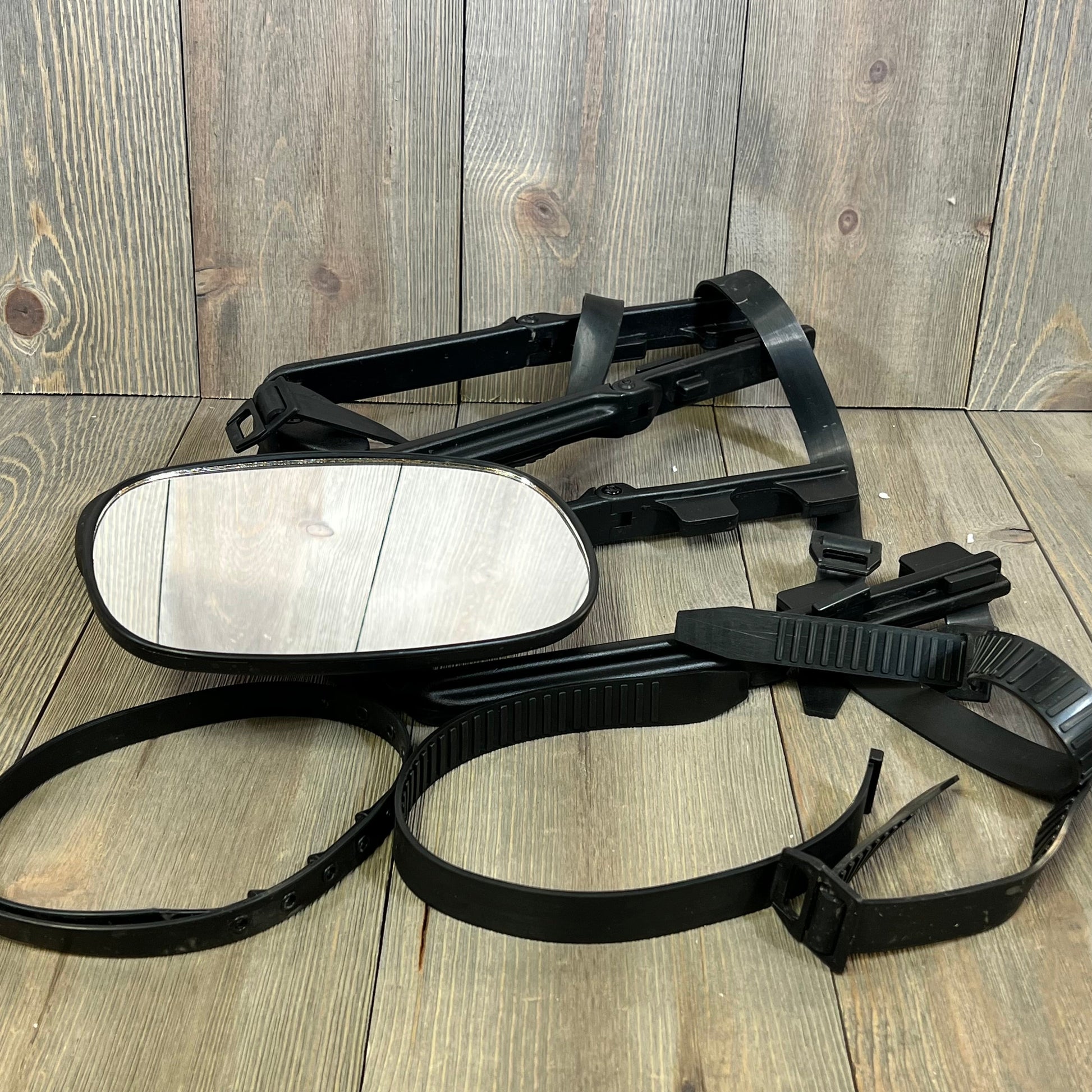 Universal clip-on towing mirror with extenders for pickups and RVs, laid on wooden surface, showcasing adjustable straps.