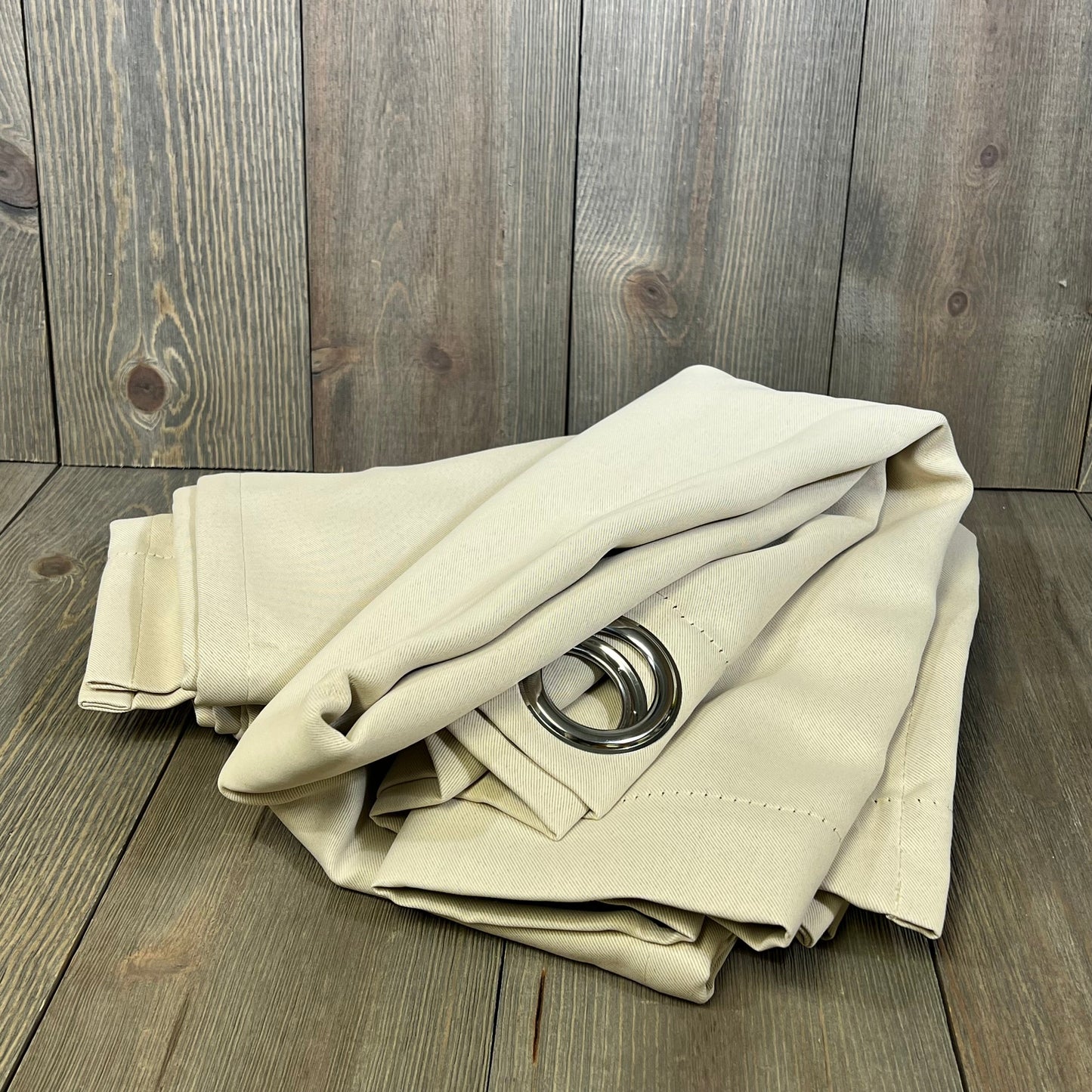 Champagne blackout curtains with grommets, folded, showcasing thermal insulation and light-blocking fabric on wooden background.