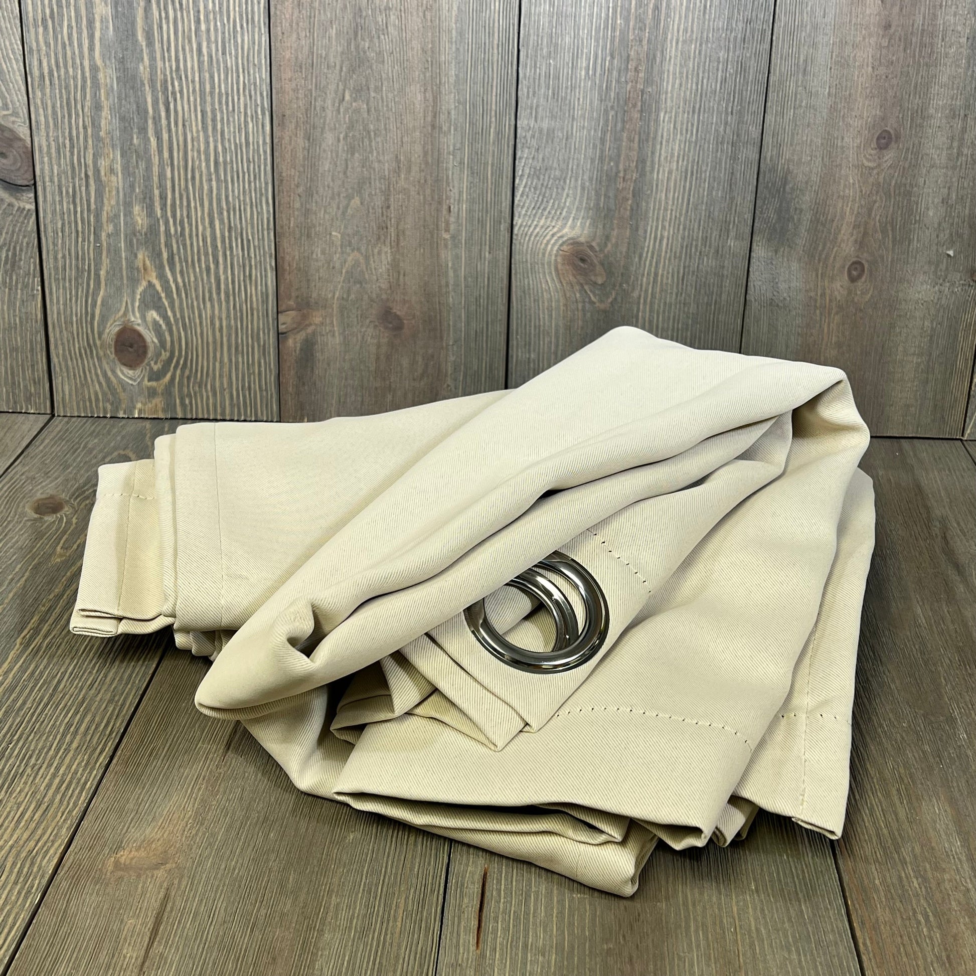 Champagne blackout curtains with grommets, folded, showcasing thermal insulation and light-blocking fabric on wooden background.