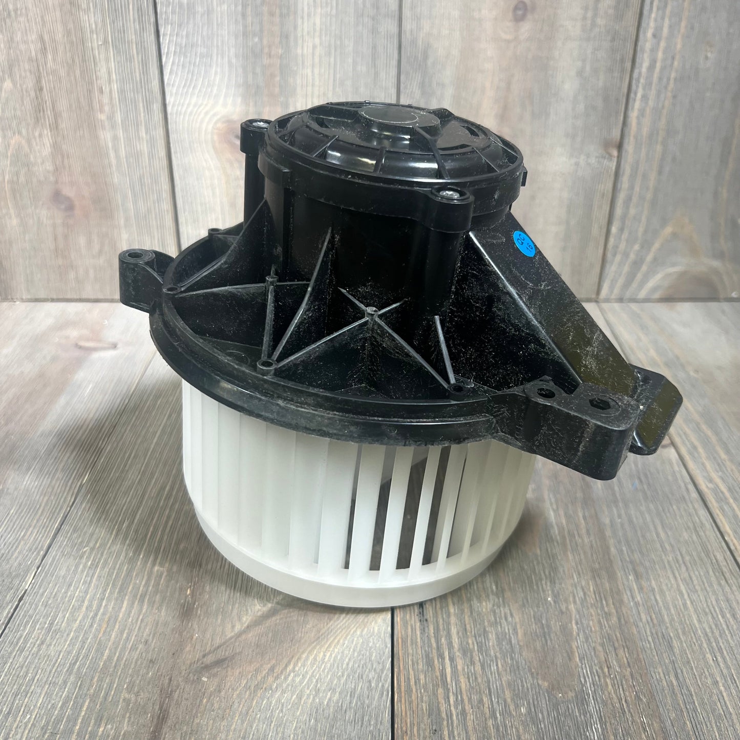 HVAC plastic heater blower motor with ABS fan cage for 2006-2009 Ford Fusion, shown on a wooden surface.