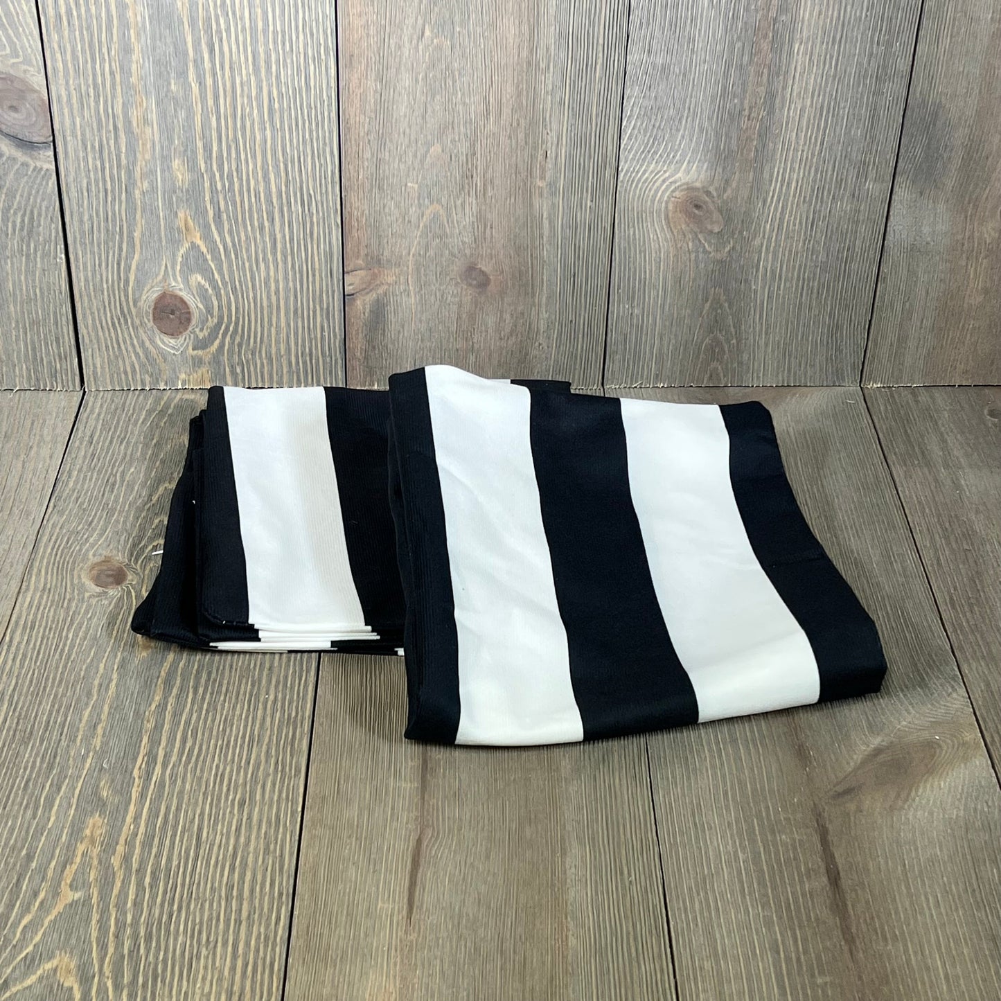 Black and white striped throw pillowcases, folded on a wooden surface, made of durable cotton polyester.