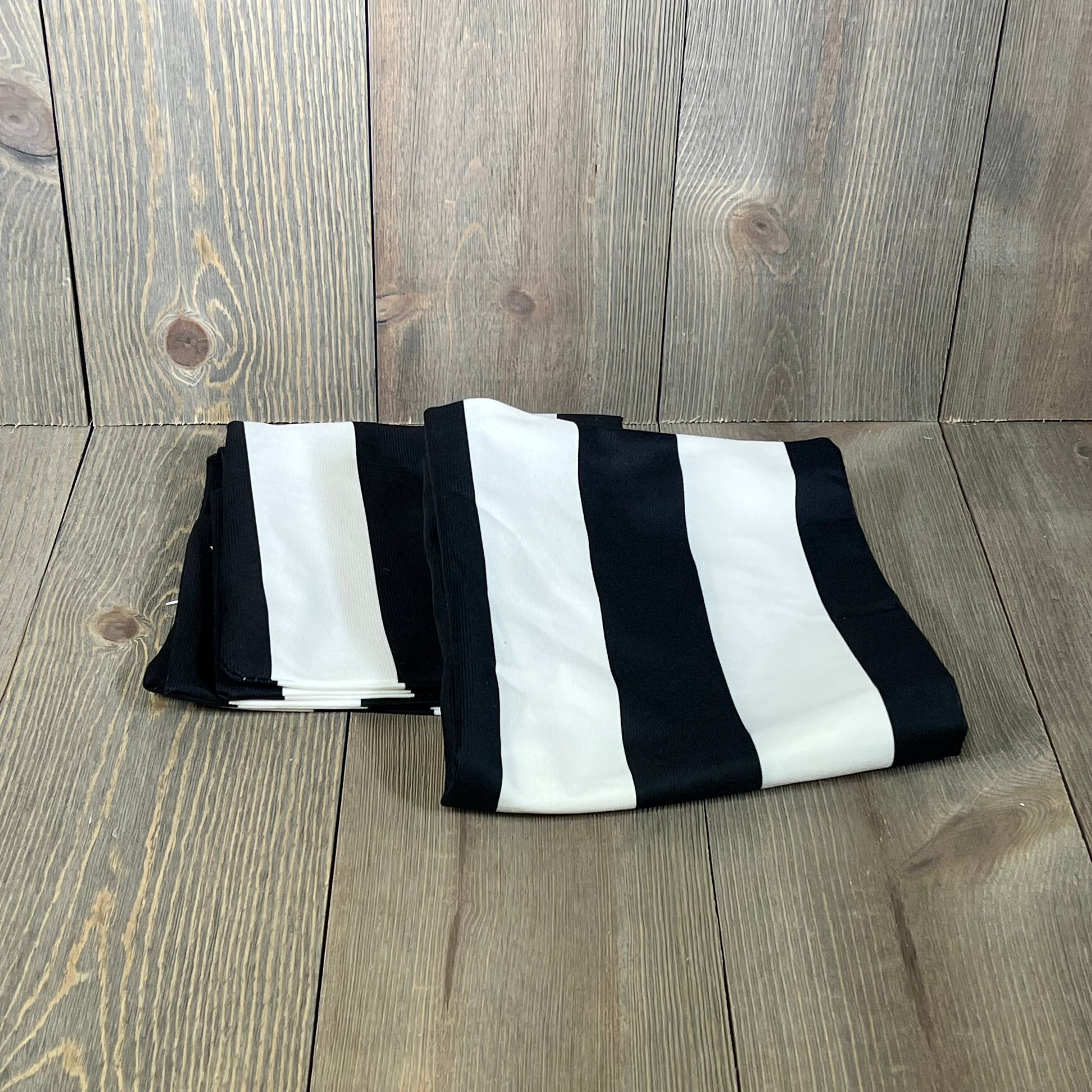 Black and white striped throw pillowcases, folded on a wooden surface, made of durable cotton polyester.