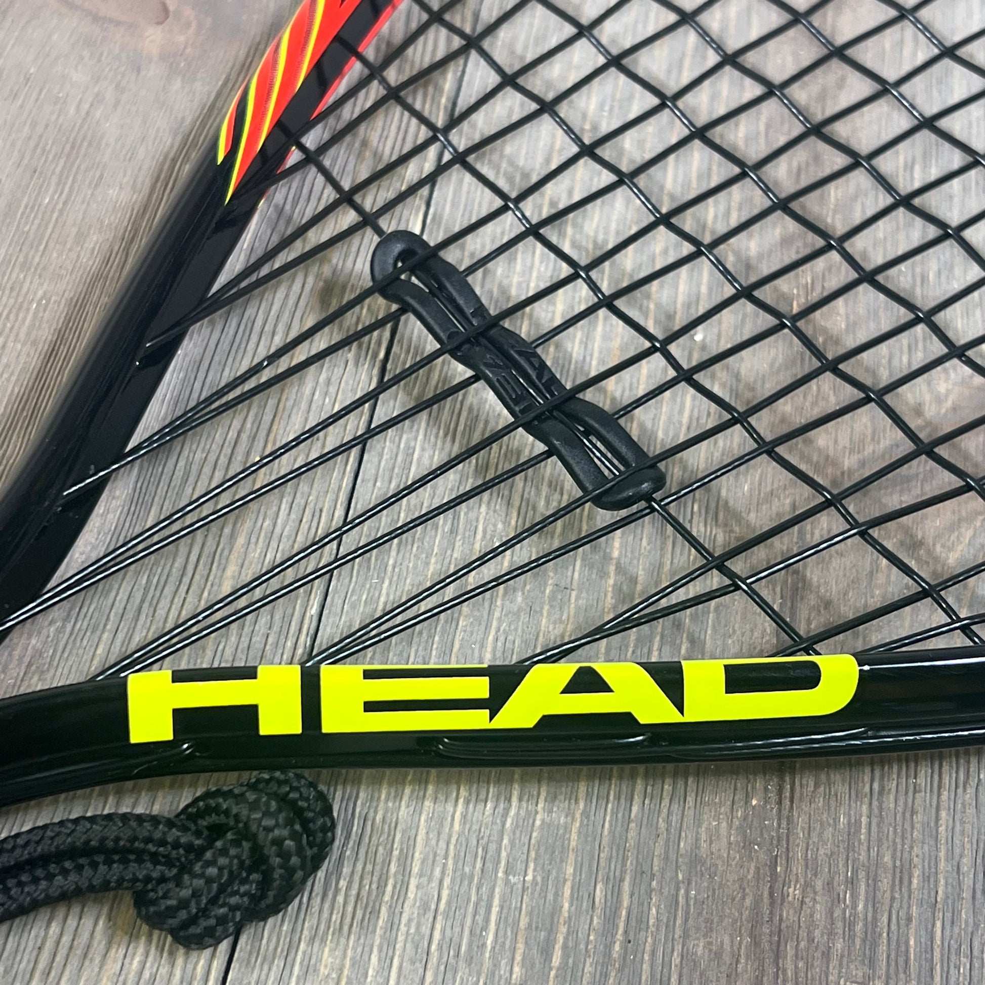 Close-up of HEAD CPS Heat Racquetball Racquet strings and frame, showcasing durable construction and vibrant logo design.