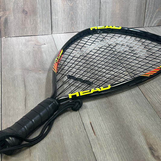 HEAD CPS Heat Racquetball Racquet with black frame, vibrant yellow accents, and textured grip on wooden floor.
