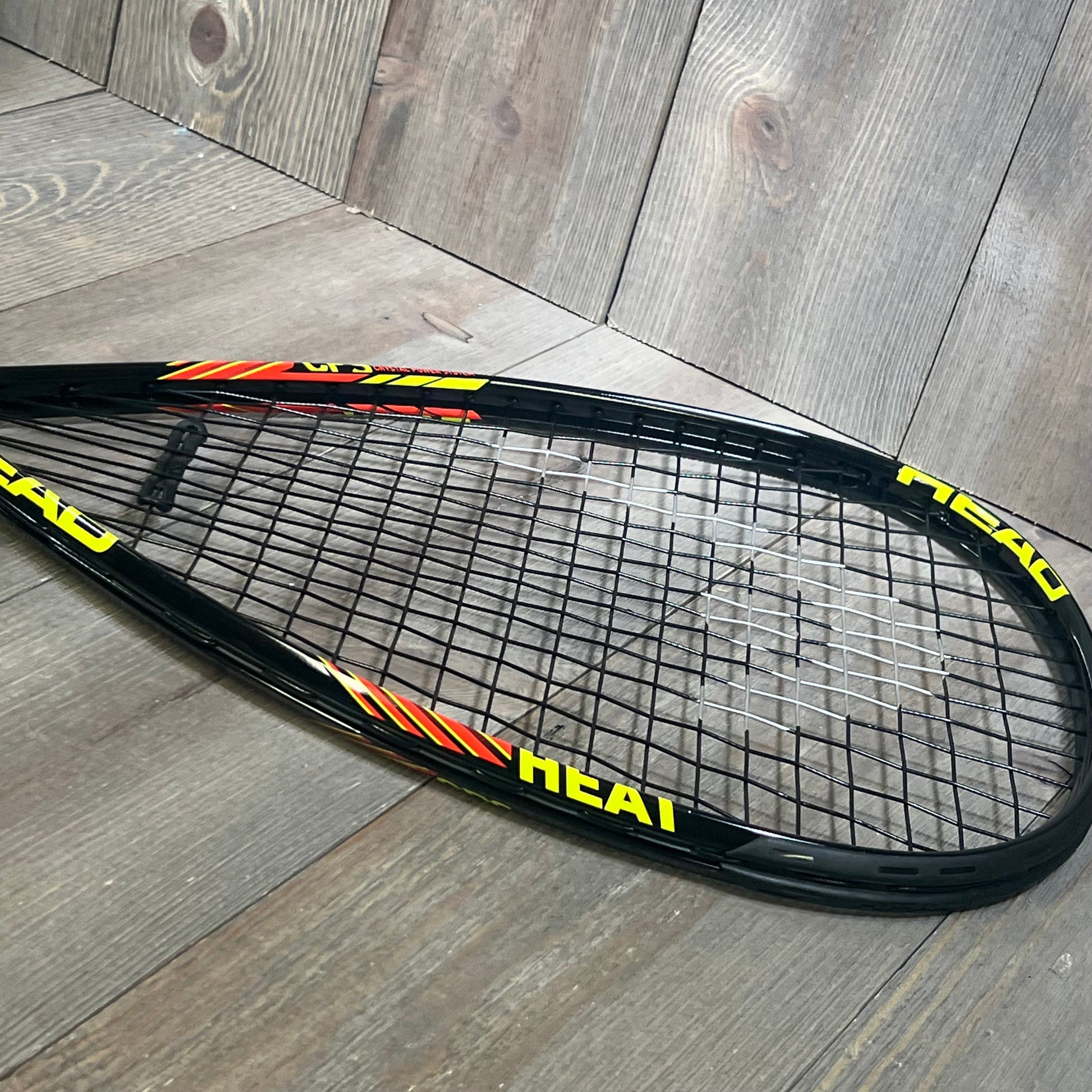 Black and yellow HEAD CPS Heat Racquetball Racquet with sleek frame design resting on a wooden floor.