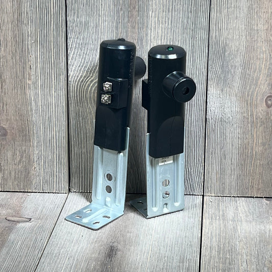 Black Genie Safe-T-Beam Replacement Kit with sender and receiver, designed for garage door safety, on a wooden background.
