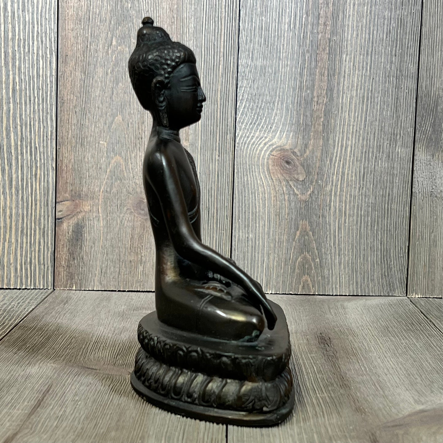Bronze Gautama Buddha statue in meditation pose, side view on wooden background.