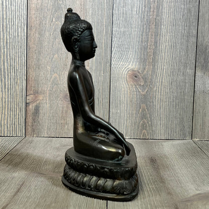 Bronze Gautama Buddha statue in meditation pose, side view on wooden background.