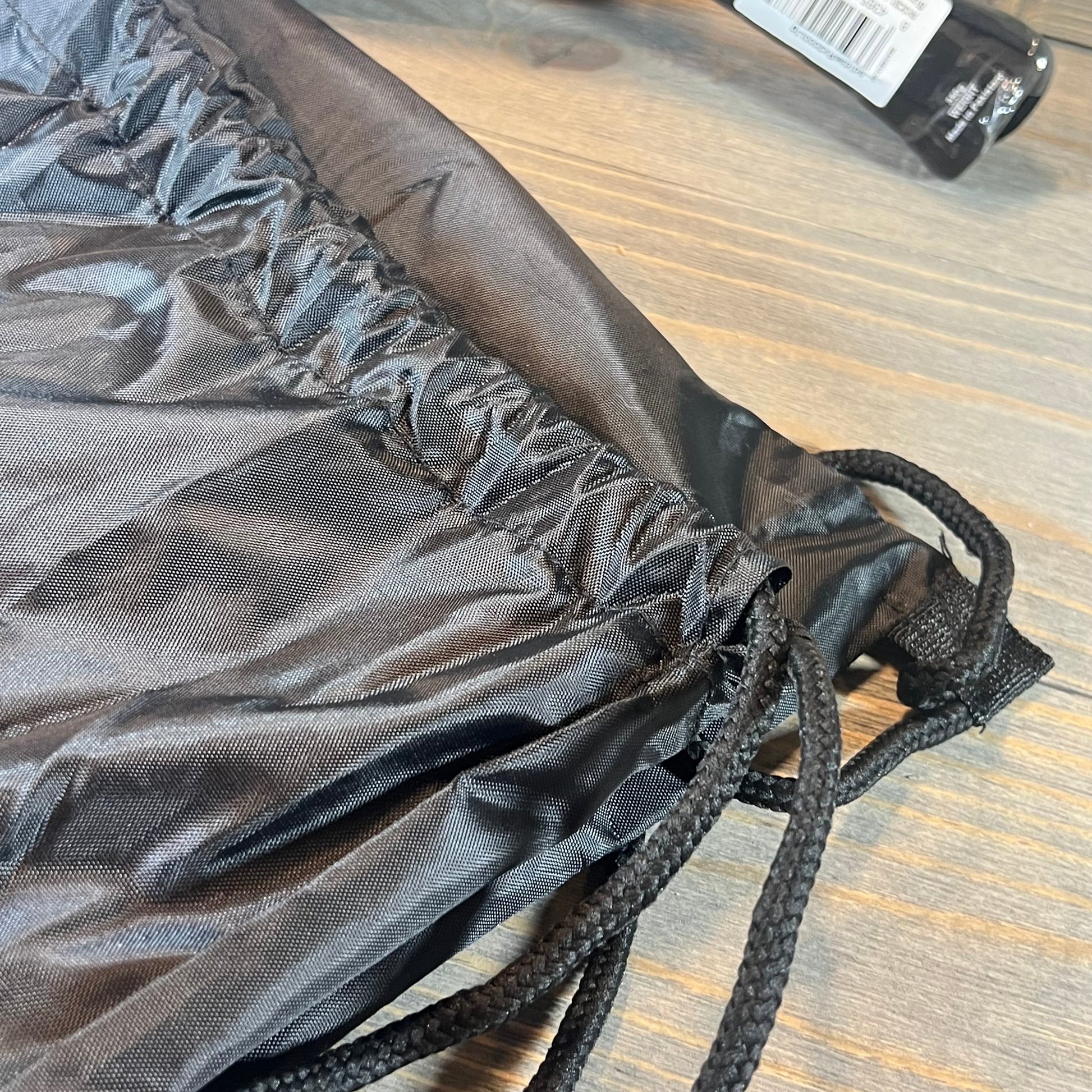 Black drawstring bag for Adidas RX 2000 Light blue padel racket, showcasing durable fabric and sturdy cords on wood surface.