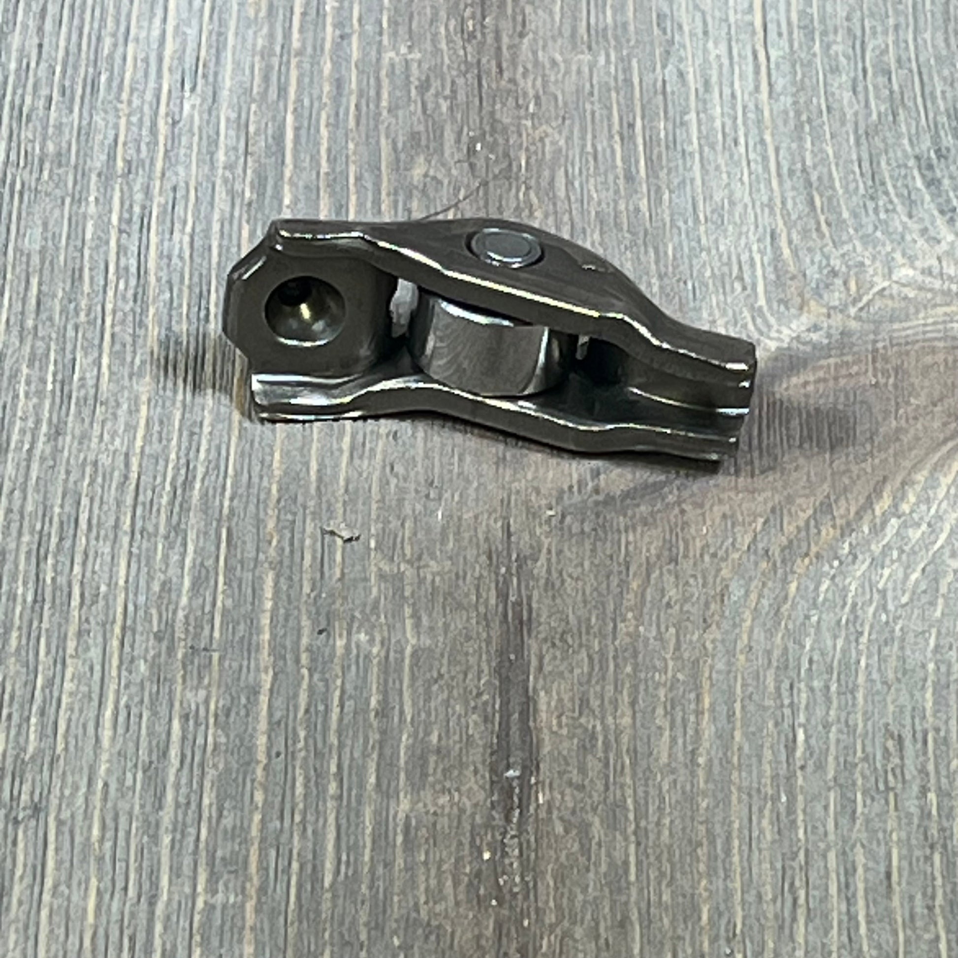 Ford 3L3Z-6564-BA rocker arm valve assembly on wooden surface, showcasing sturdy metal construction.