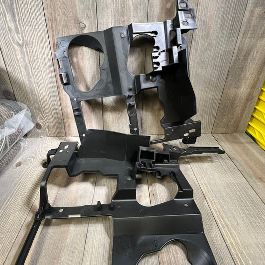 Black headlight bracket mounting panels for Chevy Silverado 1999-2006, shown on a wooden surface, driver and passenger side.