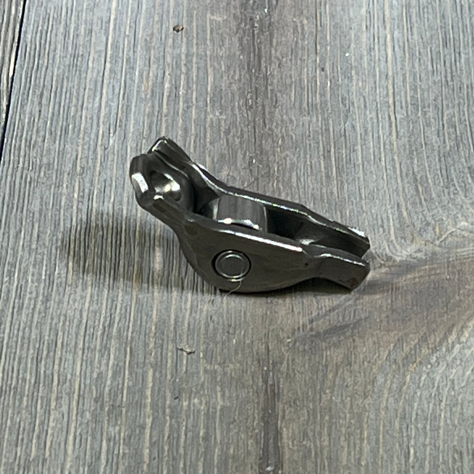 Ford 3L3Z-6564-BA Rocker Arm Valve Assembly on wooden surface, showcasing durable metal construction.