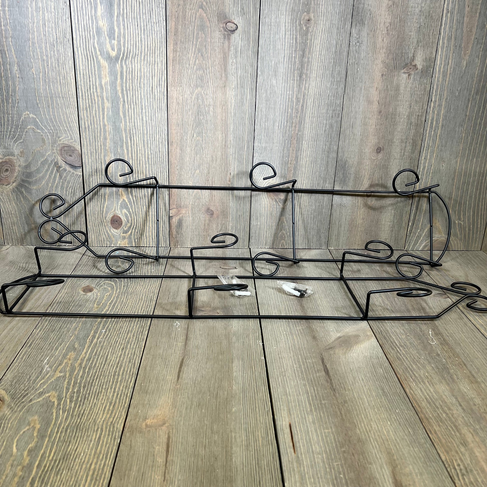 Black 3-tier vertical wall plate holder with scroll design, perfect for displaying decorative dishes on wooden background.