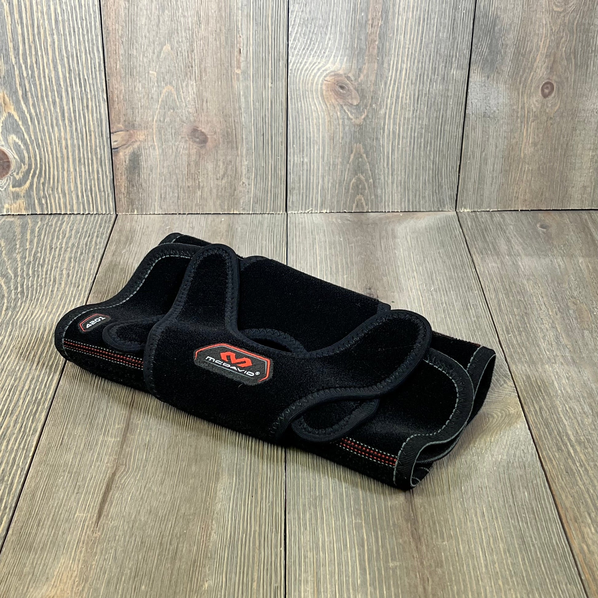 Black McDavid MD4201 knee wrap with stays, small size, offering versatile support and comfort on a wooden surface.