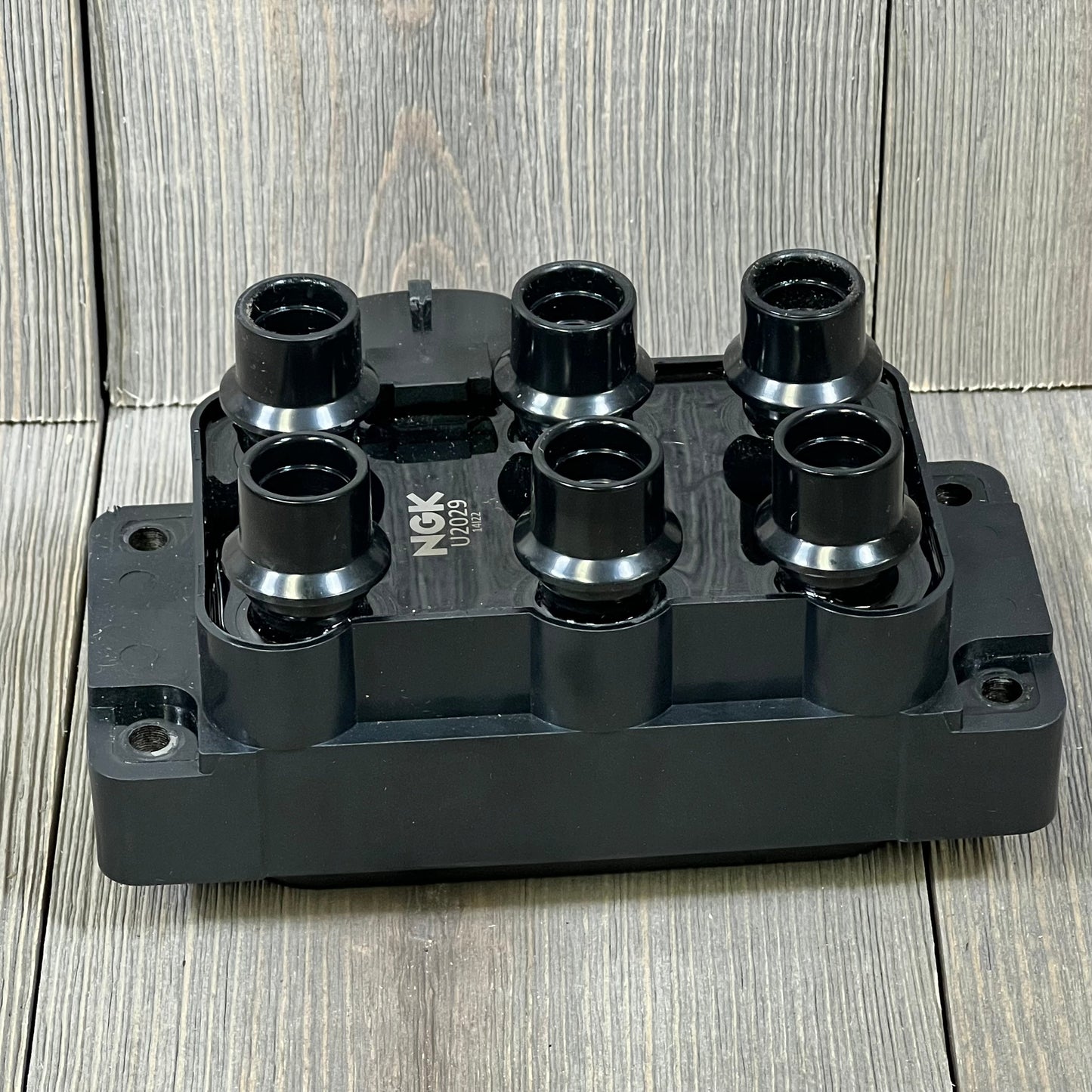 NGK U2029 (48806) ignition coil for distributorless ignition system on wooden background, showcasing six black connectors.
