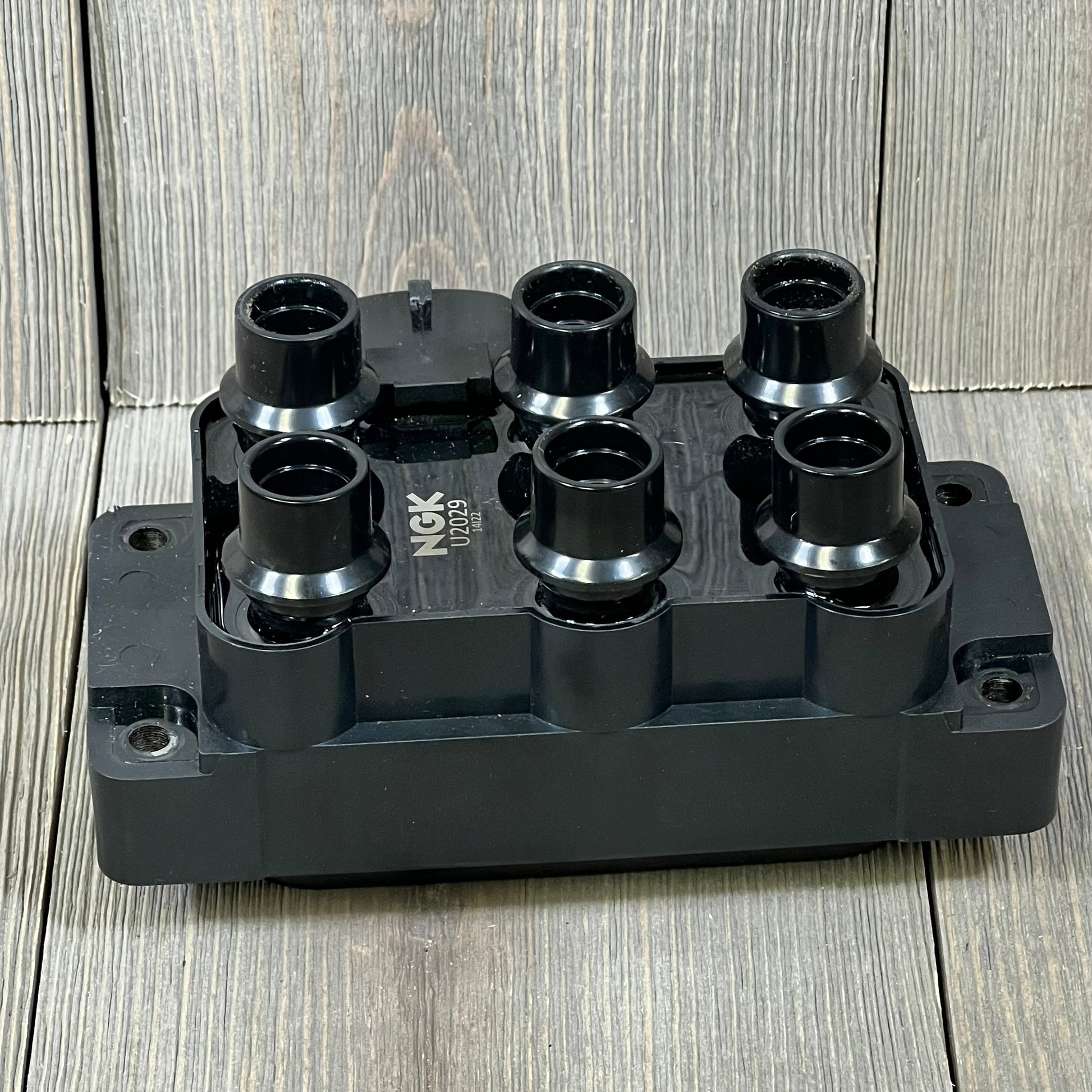 NGK U2029 (48806) ignition coil for distributorless ignition system on wooden background, showcasing six black connectors.