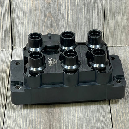 NGK U2029 (48806) ignition coil for distributorless ignition system on wooden background, showcasing six black connectors.