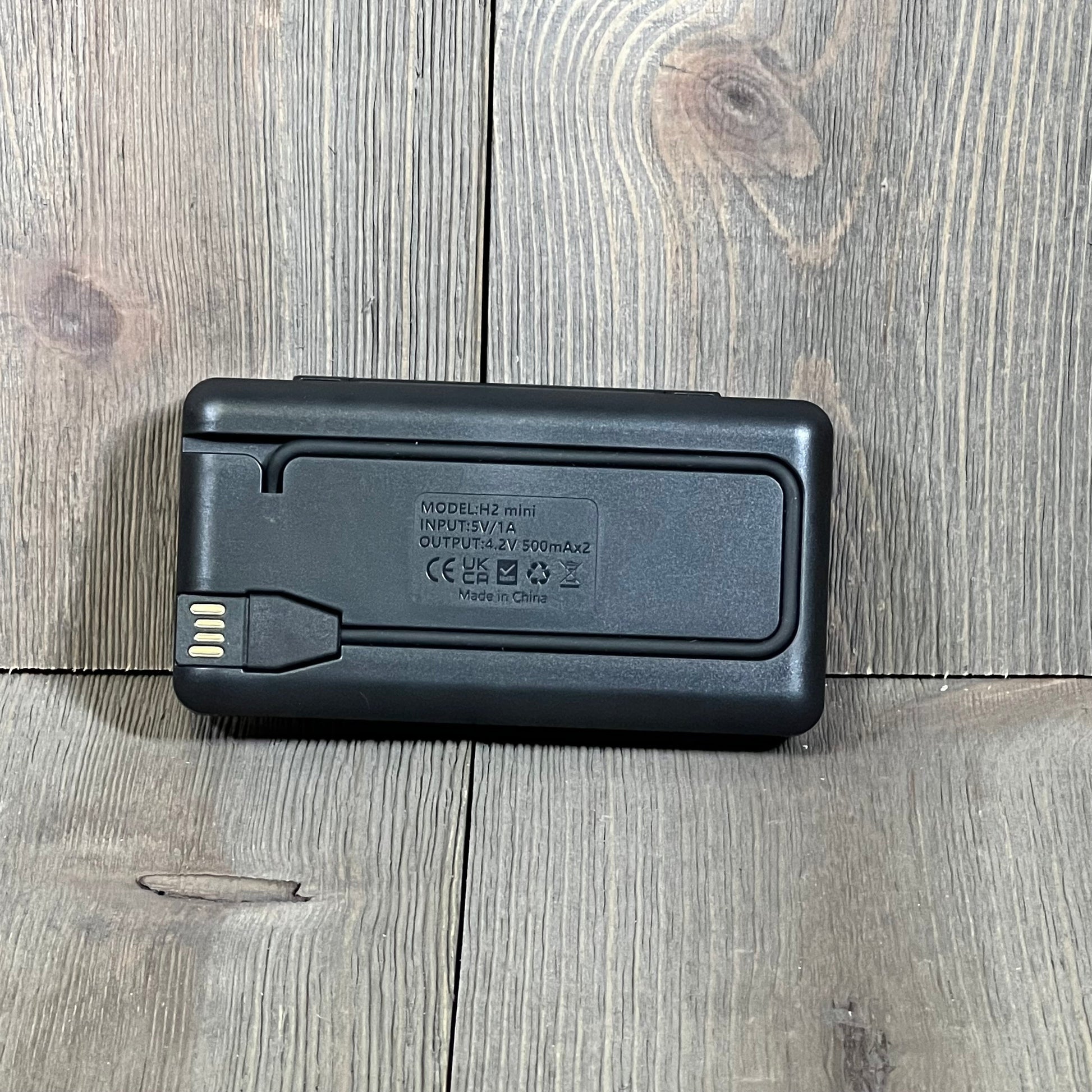Black NP-BN1 battery charger for Sony cameras, compatible with DSC-WX500 and WX530, placed on a wooden surface.