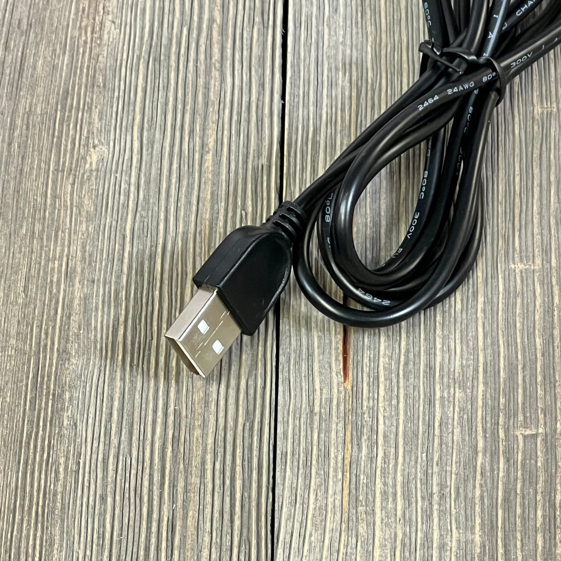 Black USB cable for LIBORA LED desk lamp, shown coiled on a wooden surface, providing easy connectivity for home office use.