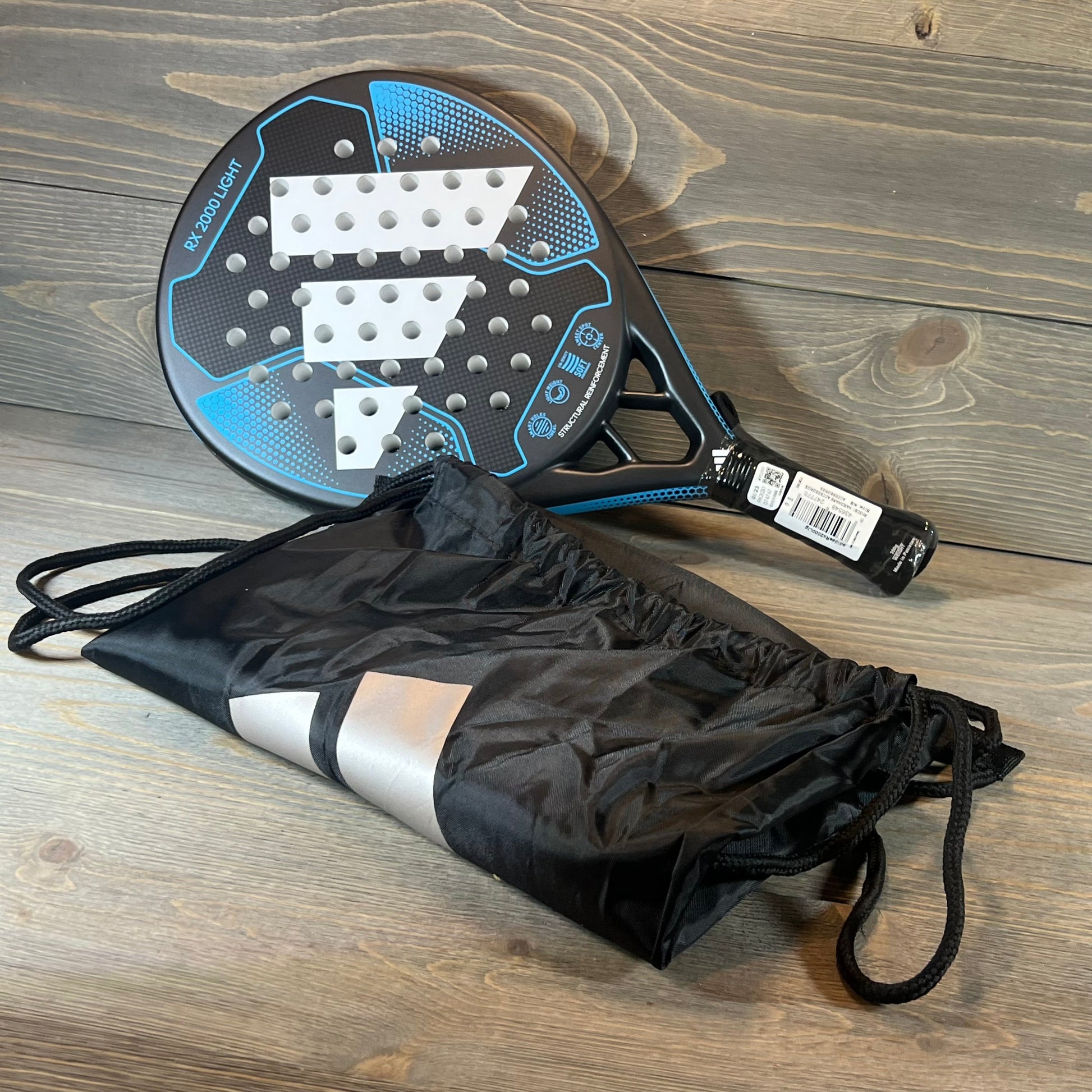 Blue Adidas RX 2000 Light padel racket with carrying bag on a wooden surface. Ideal for paddle sports enthusiasts.