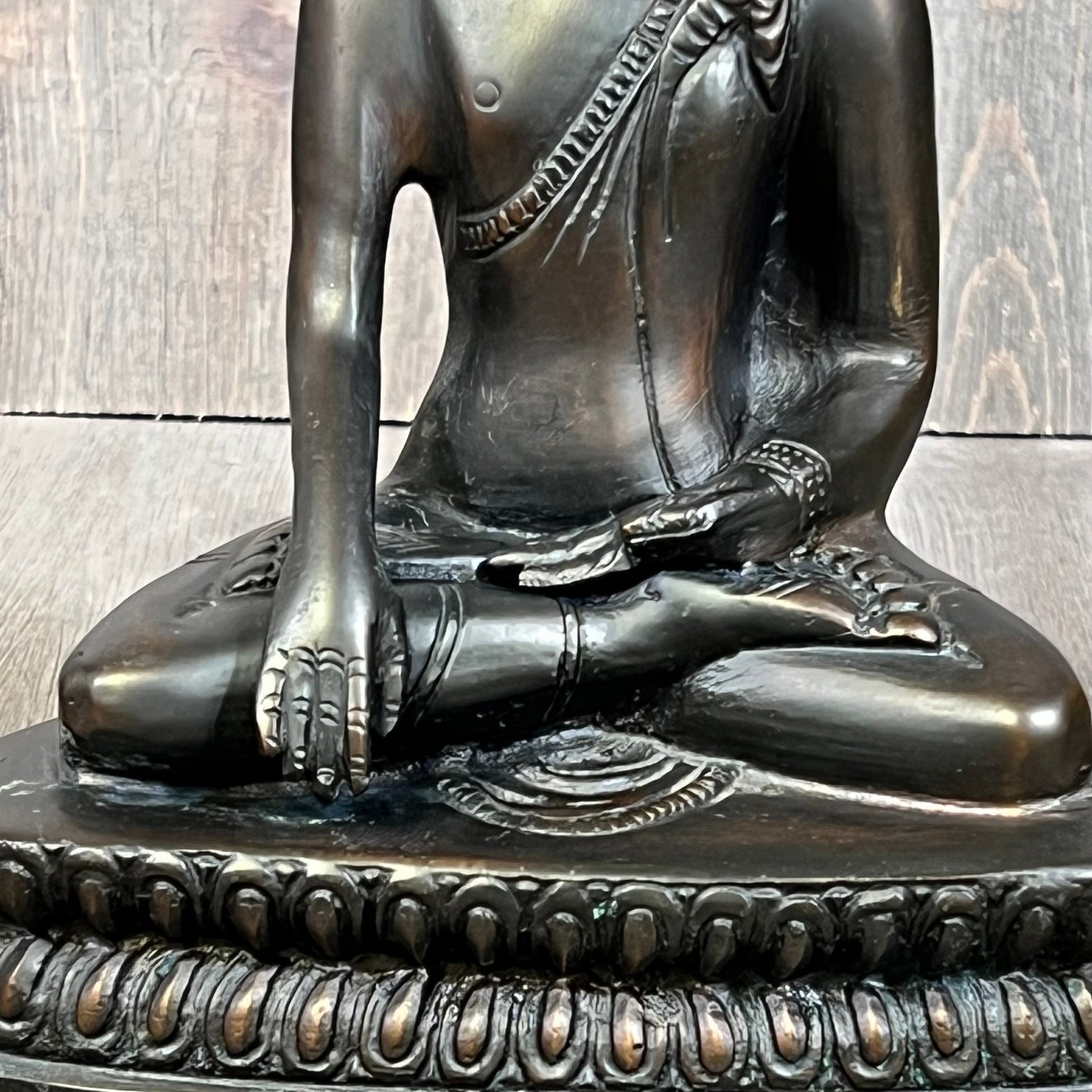 Seated bronze Gautama Buddha statue with intricate robe details, embodying peace and serenity on a carved base.