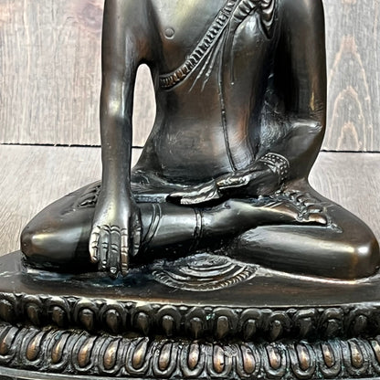Seated bronze Gautama Buddha statue with intricate robe details, embodying peace and serenity on a carved base.