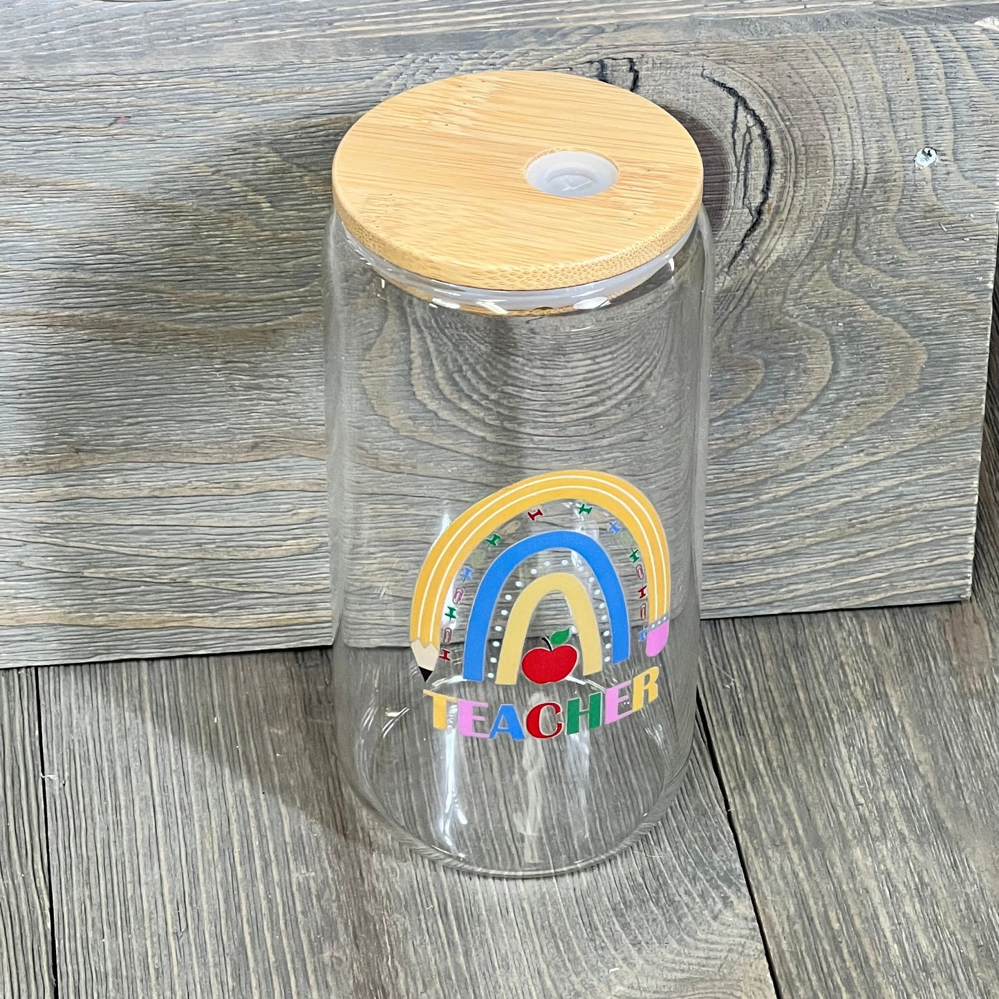 Clear glass cup with bamboo lid, decorated with a colorful rainbow and "Teacher" text. Ideal for Teacher Appreciation gifts.