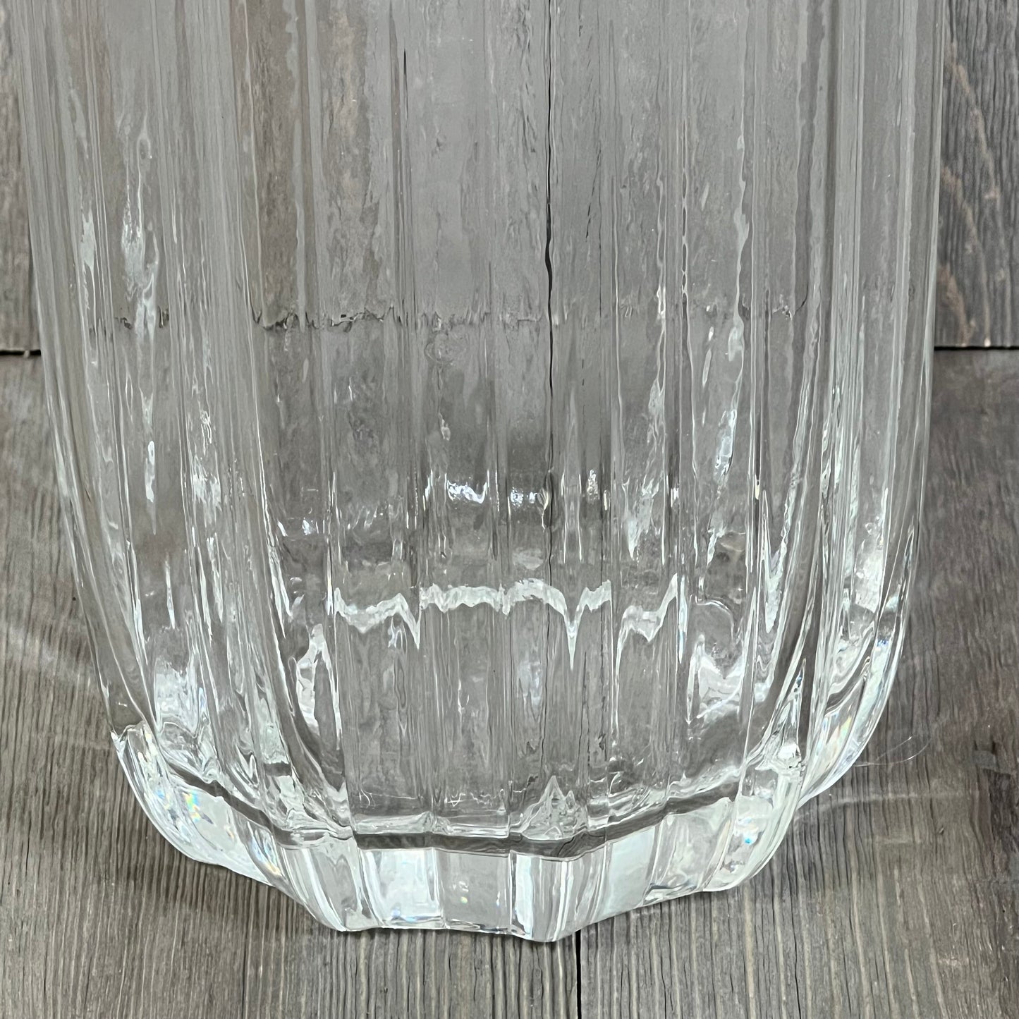 Tall clear glass vase with a simple striped design, perfect for home decor and flower arrangements, stands elegantly on a wooden floor.