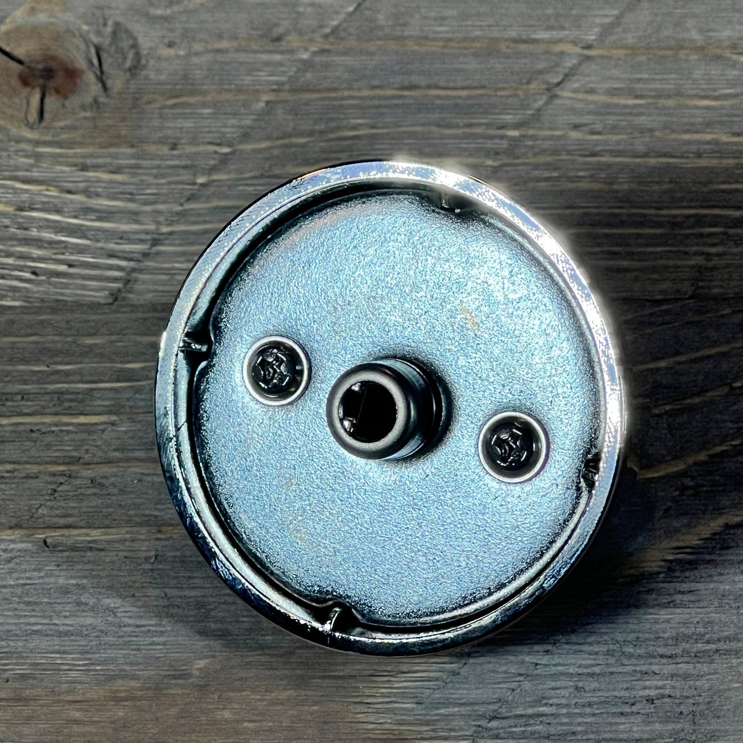 Close-up of a Samsung gas stove burner control knob, metallic finish, viewed from the back, highlighting attachment points.