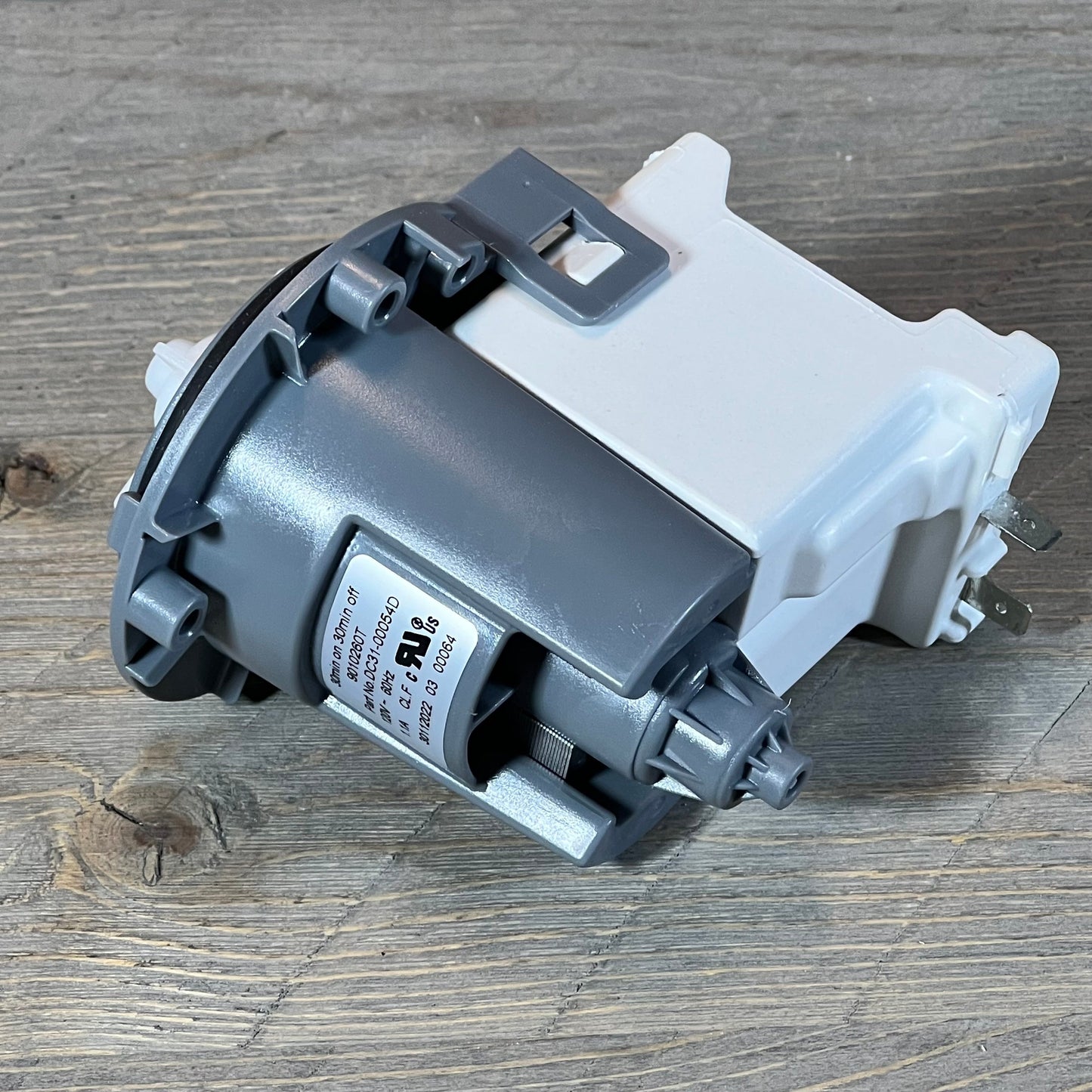 Close-up of Supco LP054D Washer Drain Pump, compatible with Samsung models, displayed on a wooden surface.