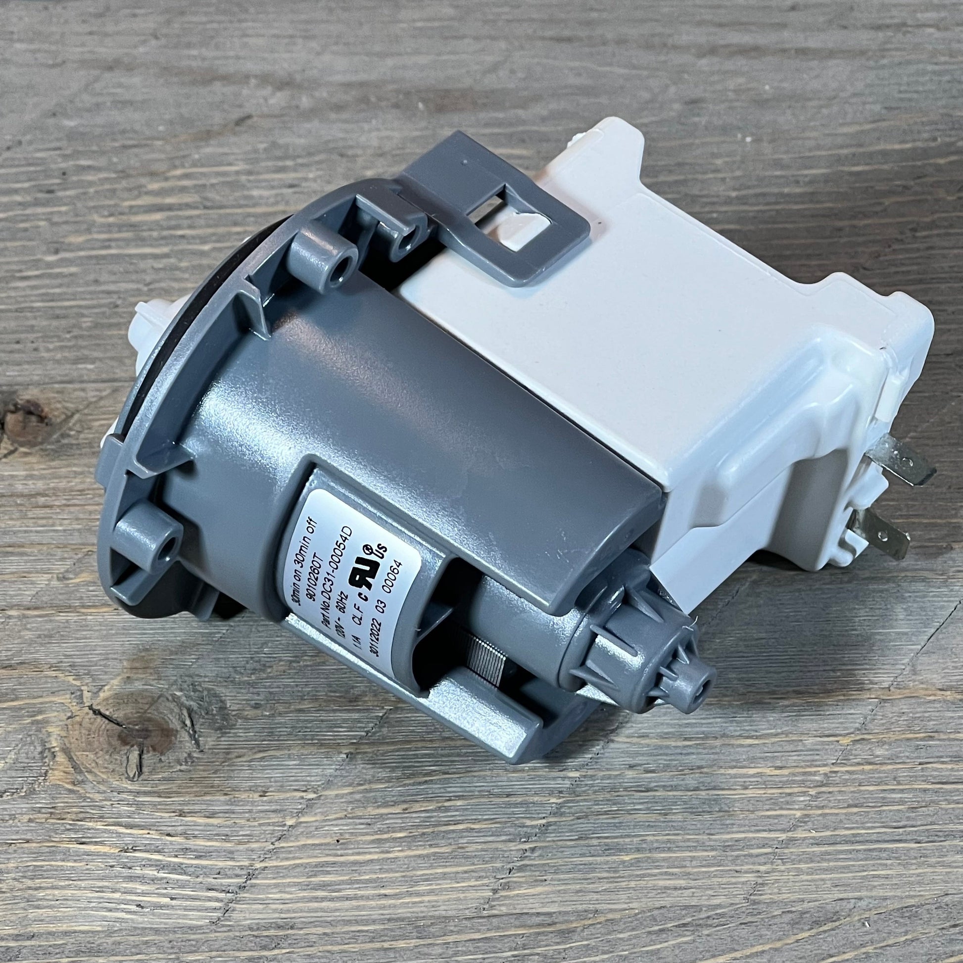 Close-up of Supco LP054D Washer Drain Pump, compatible with Samsung models, displayed on a wooden surface.