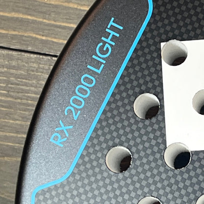 Close-up of the Adidas RX 2000 Light padel racket, showcasing the textured blue surface and precision holes.