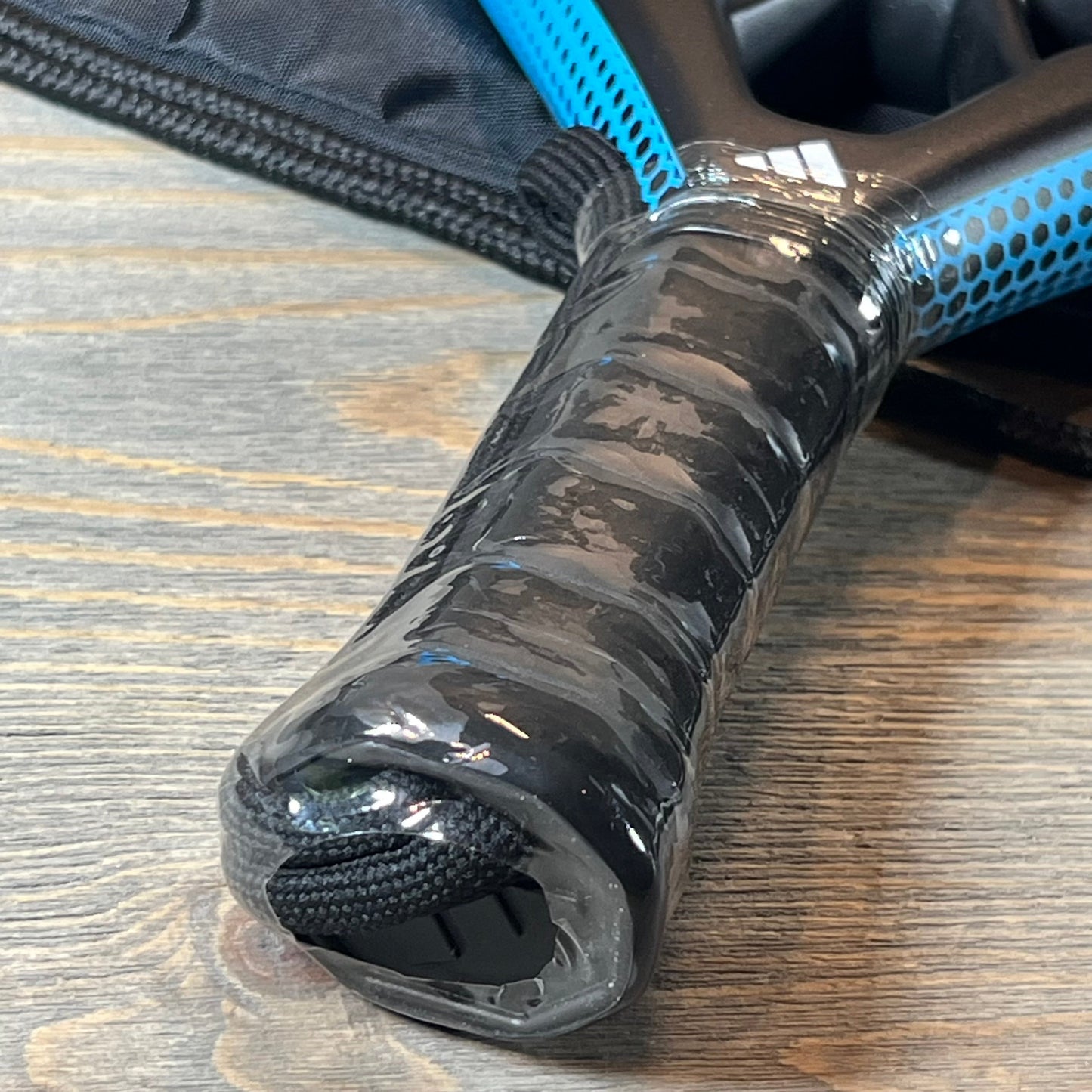 Close-up of the Adidas Rx 2000 Light padel racket handle in blue, showcasing the grip texture on a wooden surface.