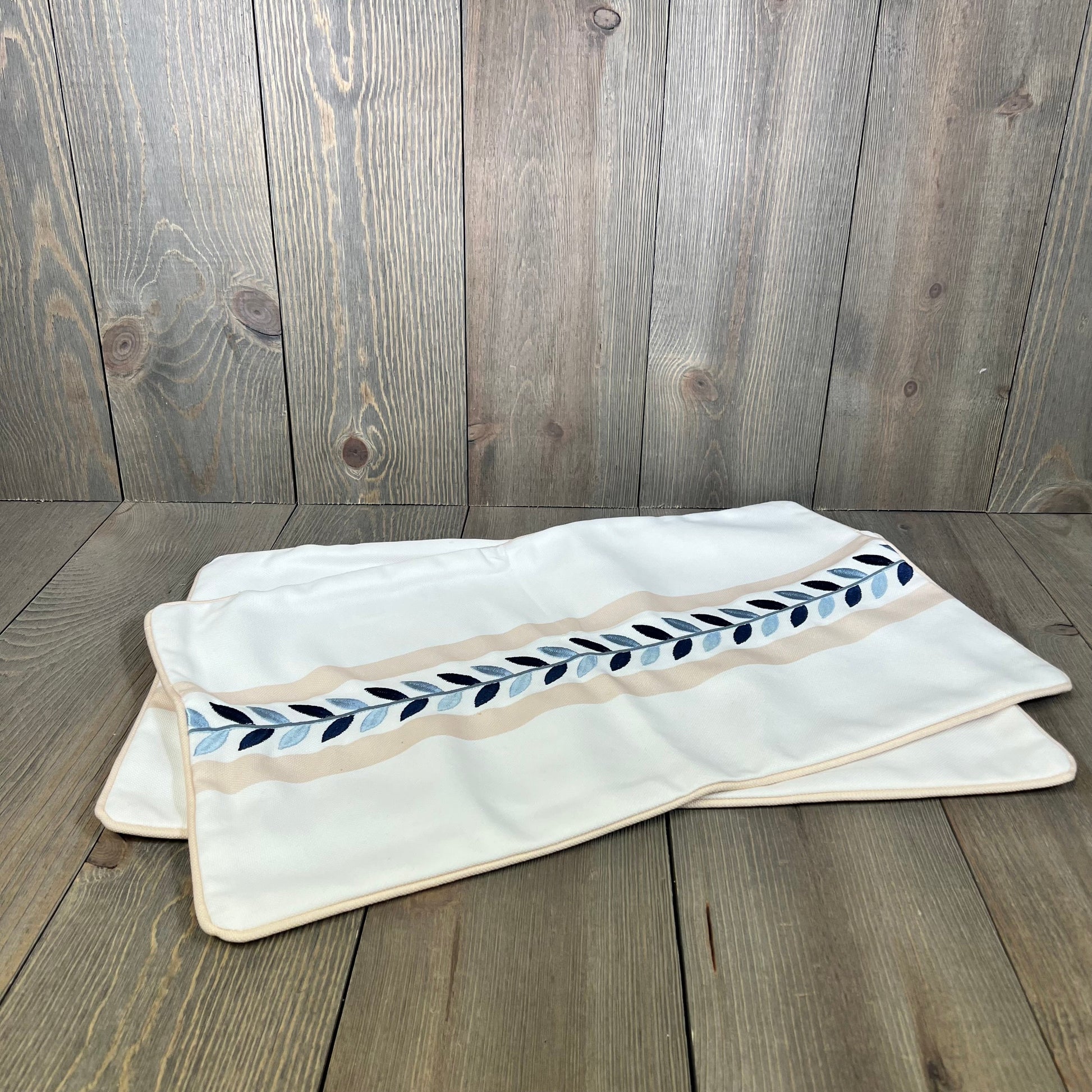 Tan lumbar pillow cover with blue leaf embroidery, perfect for patio decor, water-repellent fabric for outdoor use.
